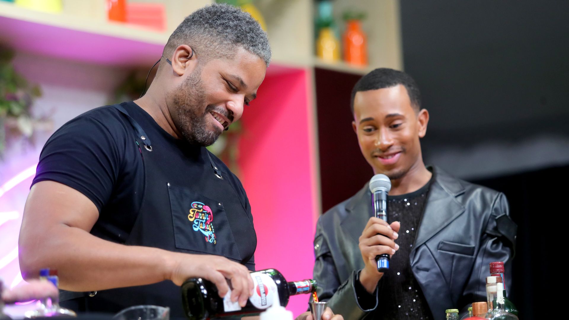 Touré Folks makes a cocktail as Kalen Allen looks on and holds a microphone.