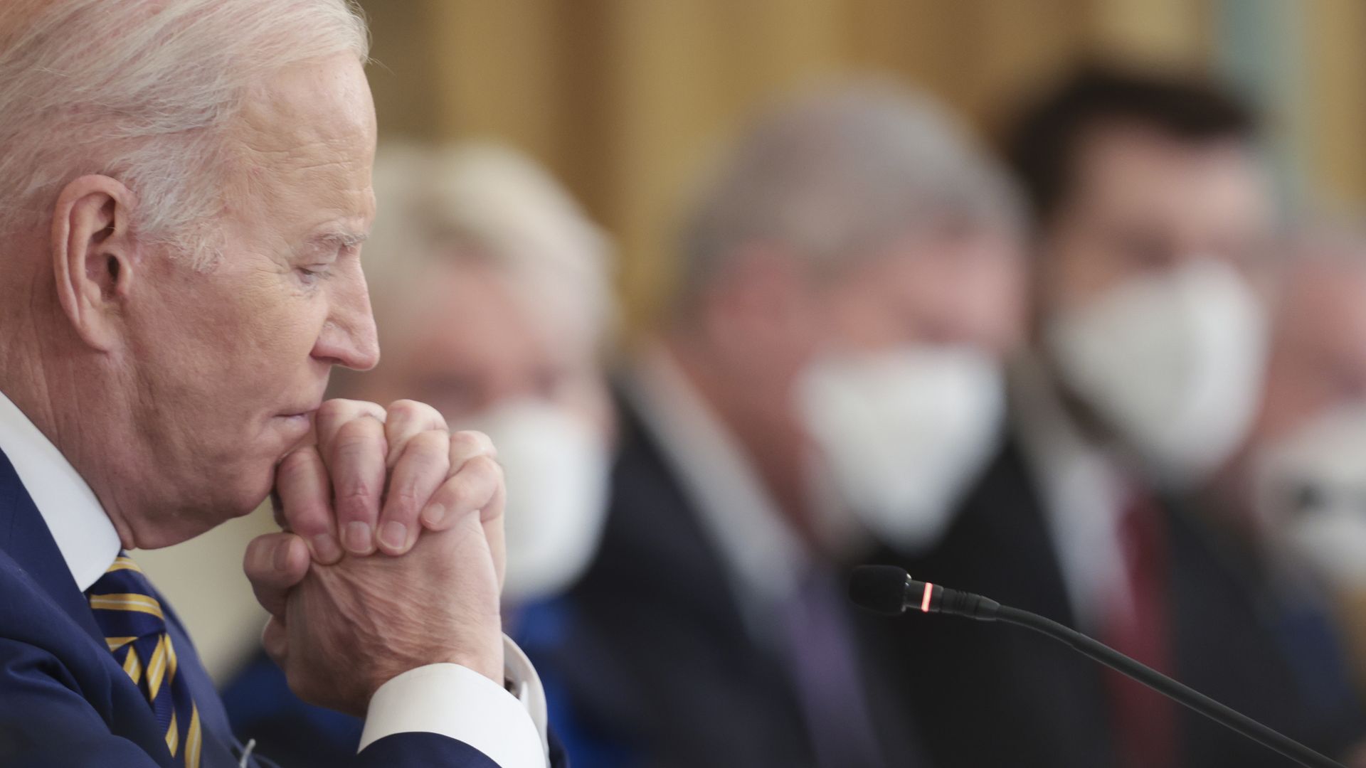 Photo of Joe Biden from the side as he rests his chin on clasped hands at a meeting