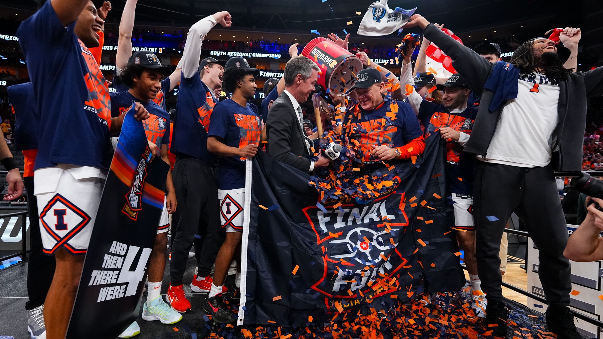 Blue and orange basketball team celebrates on stage with a trophy, confetti, and a "Final Four" banner as teammates cheer.