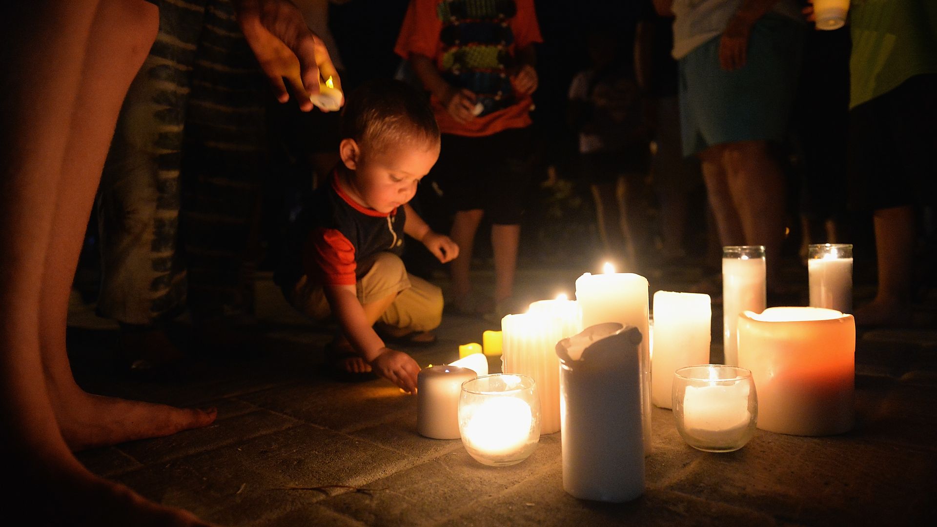 A child places a candle on the floor during a vigil. 