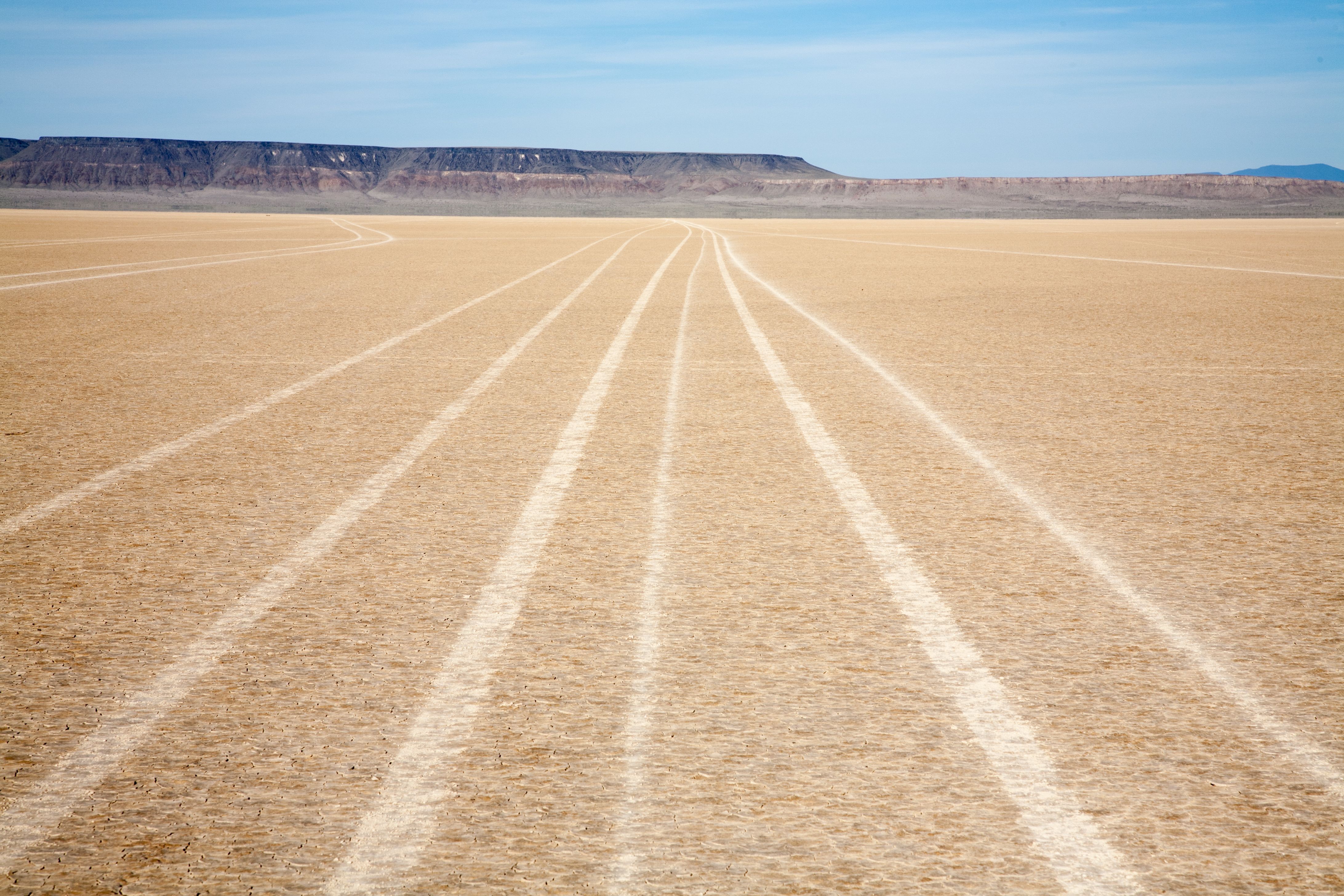 Tire tracks lead off into the distance across a flat desert landscape with hills far in the background.