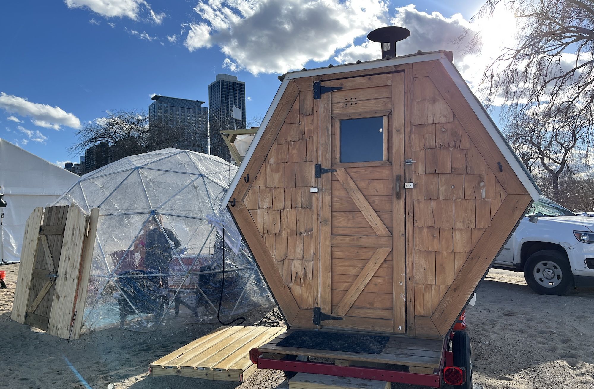 The exterior of a hexagon shaped sauna next to a clear geodesic dome.