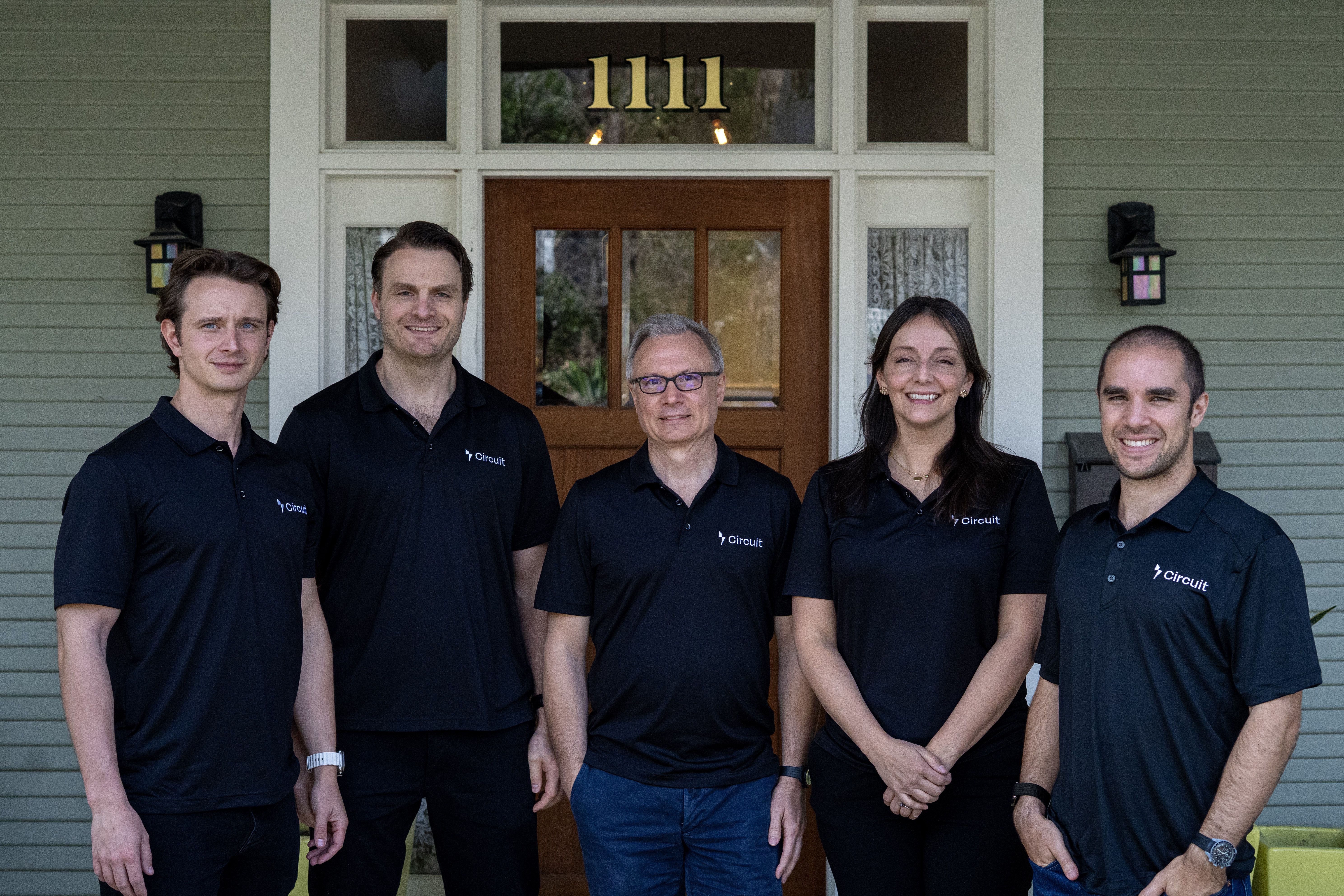 Five people wearing black Circuit-branded shirts standing in front of a doorway with the number 1111 above, smiling at the camera.