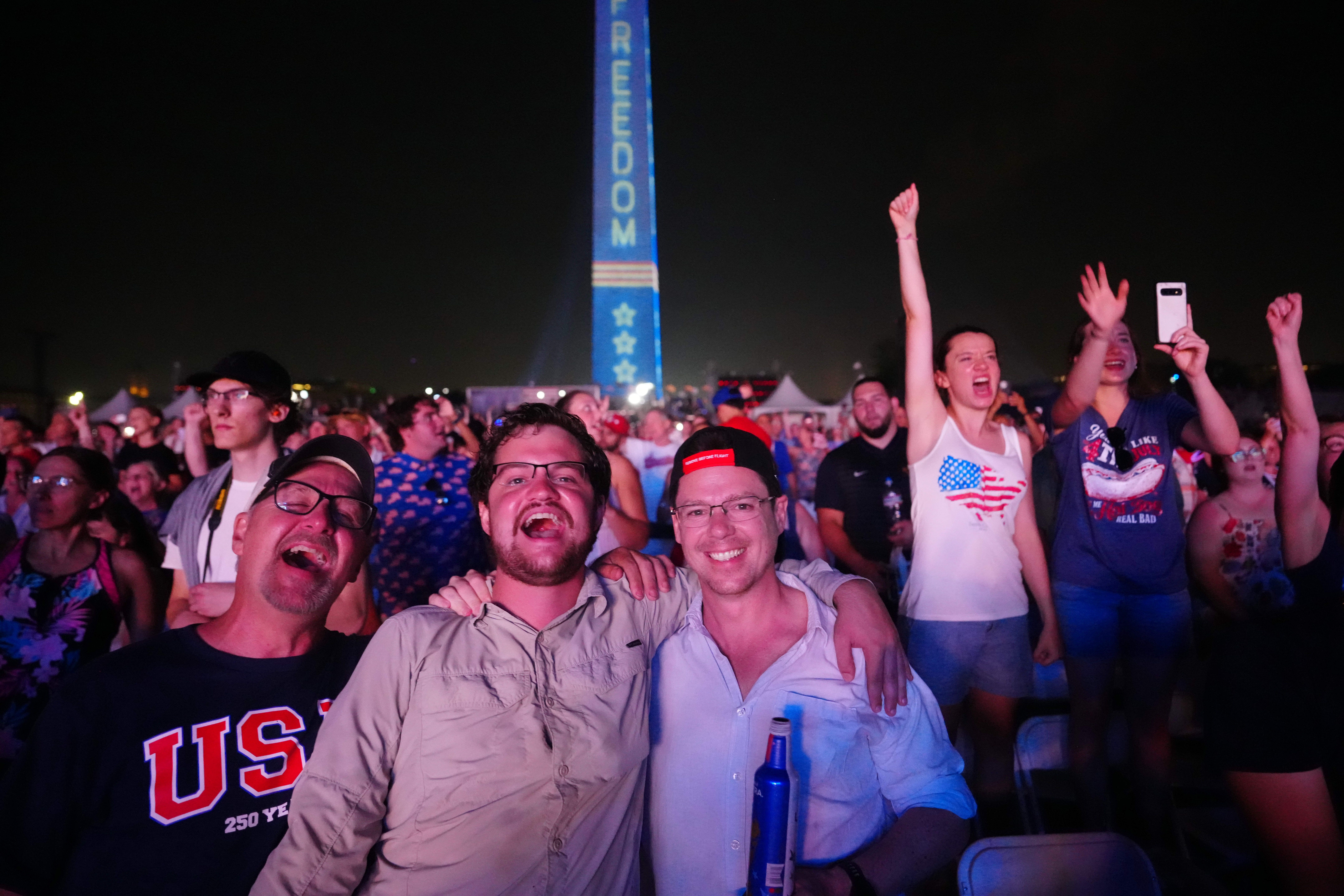 People listen to President Trump speak Saturday night on the National Mall, with "FREEDOM 250" projected on the Washington Monument.