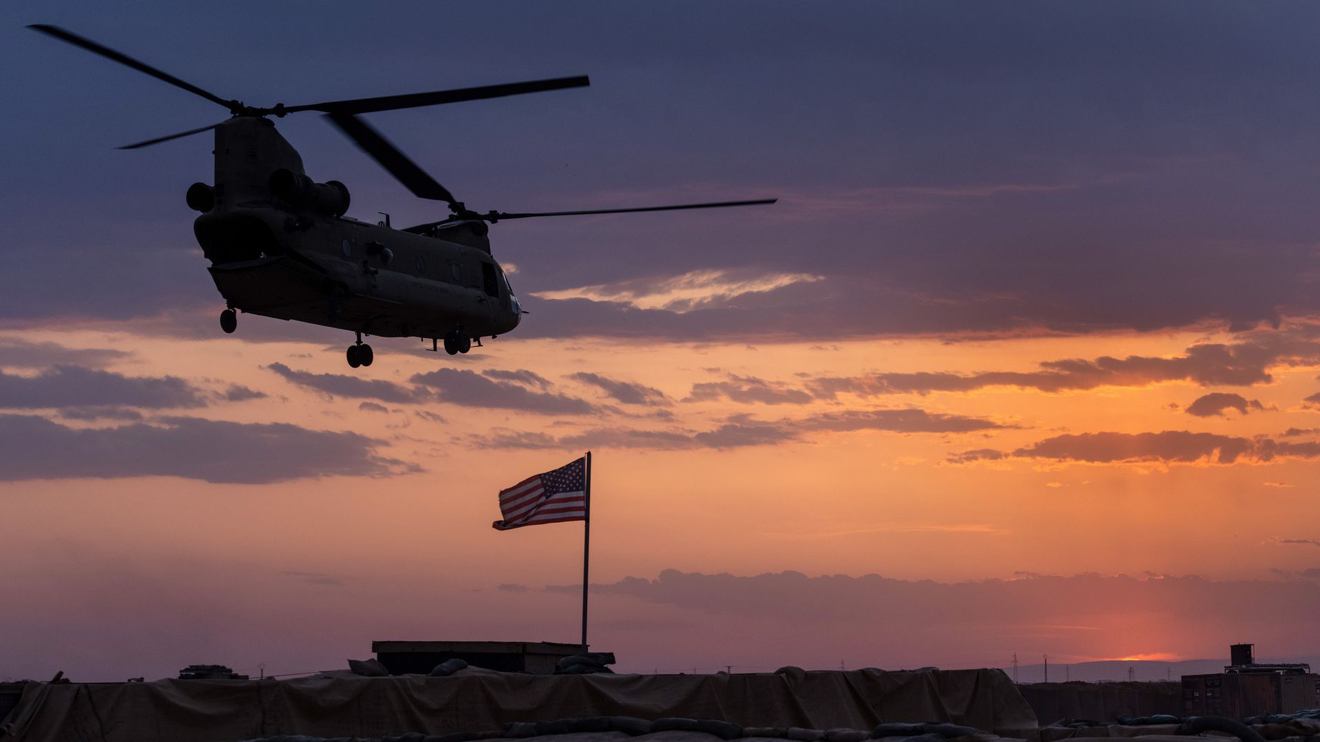Photo of a helicopter flying over a region that includes an American flag, against a sunset backdrop
