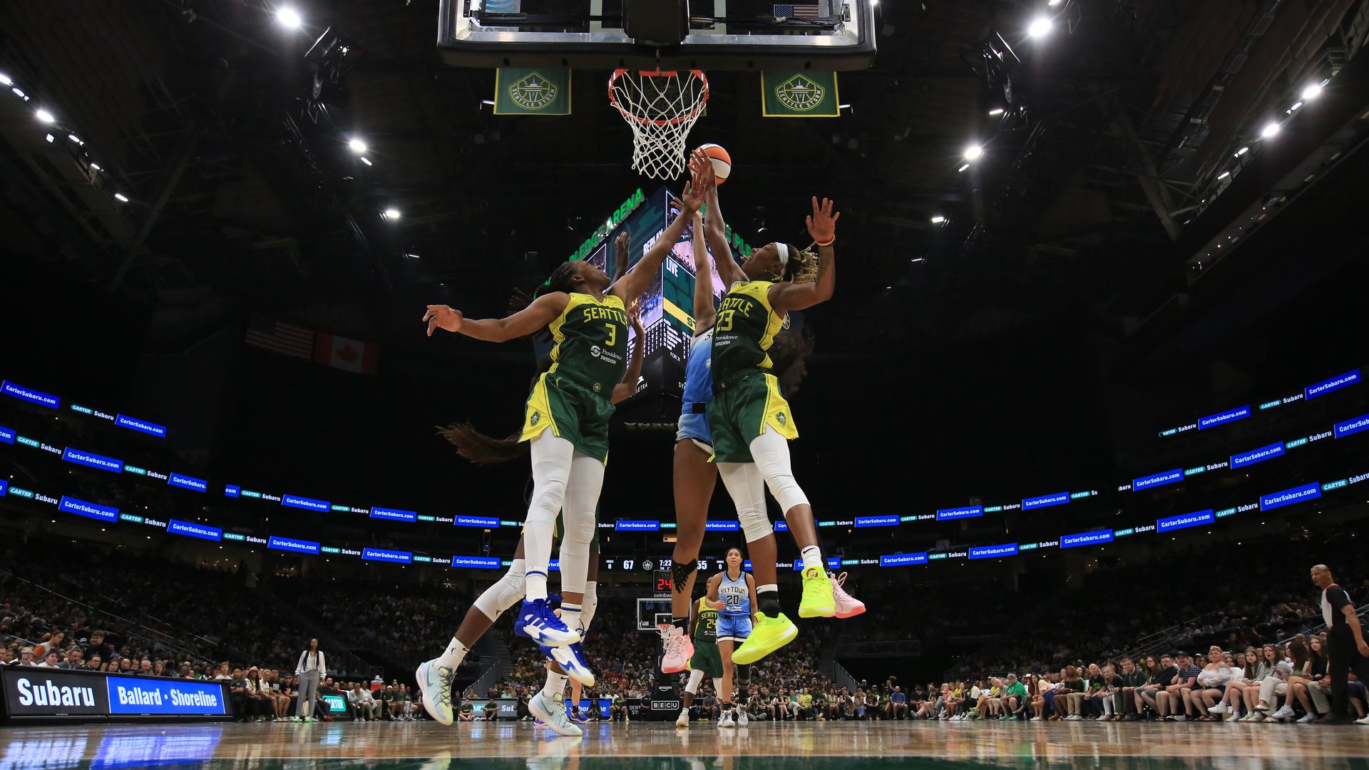 WNBA players in green and yellow leap into the air for a rebound during a Seattle Storm game. 