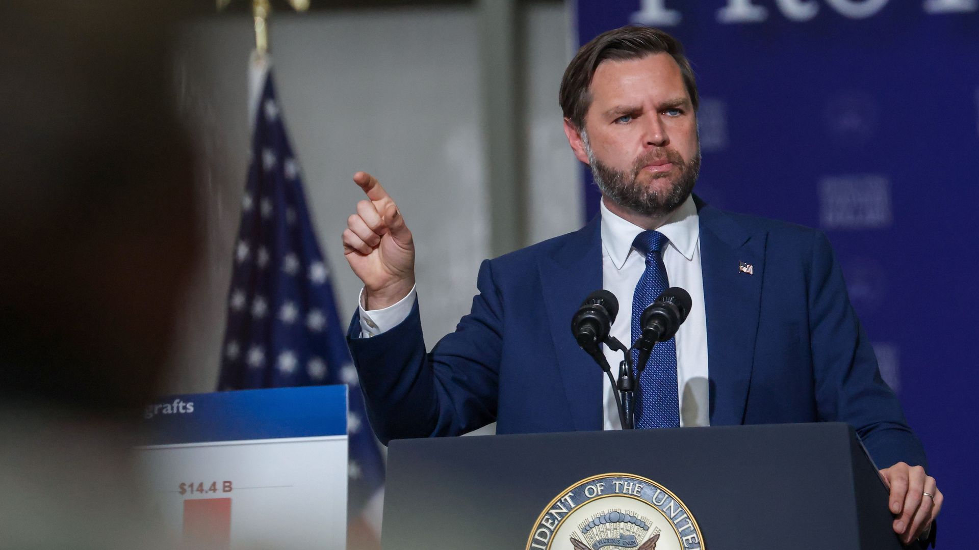 Vice President JD Vance speaks at a podium inside an aircraft hangar during an event in Milwaukee focused on the Trump administration's anti-fraud efforts.