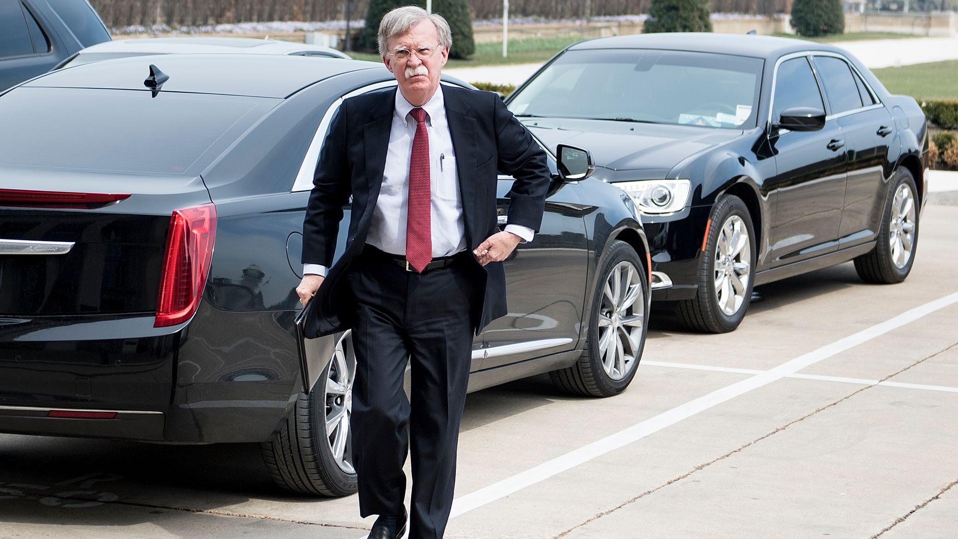 John Bolton in front of black cars