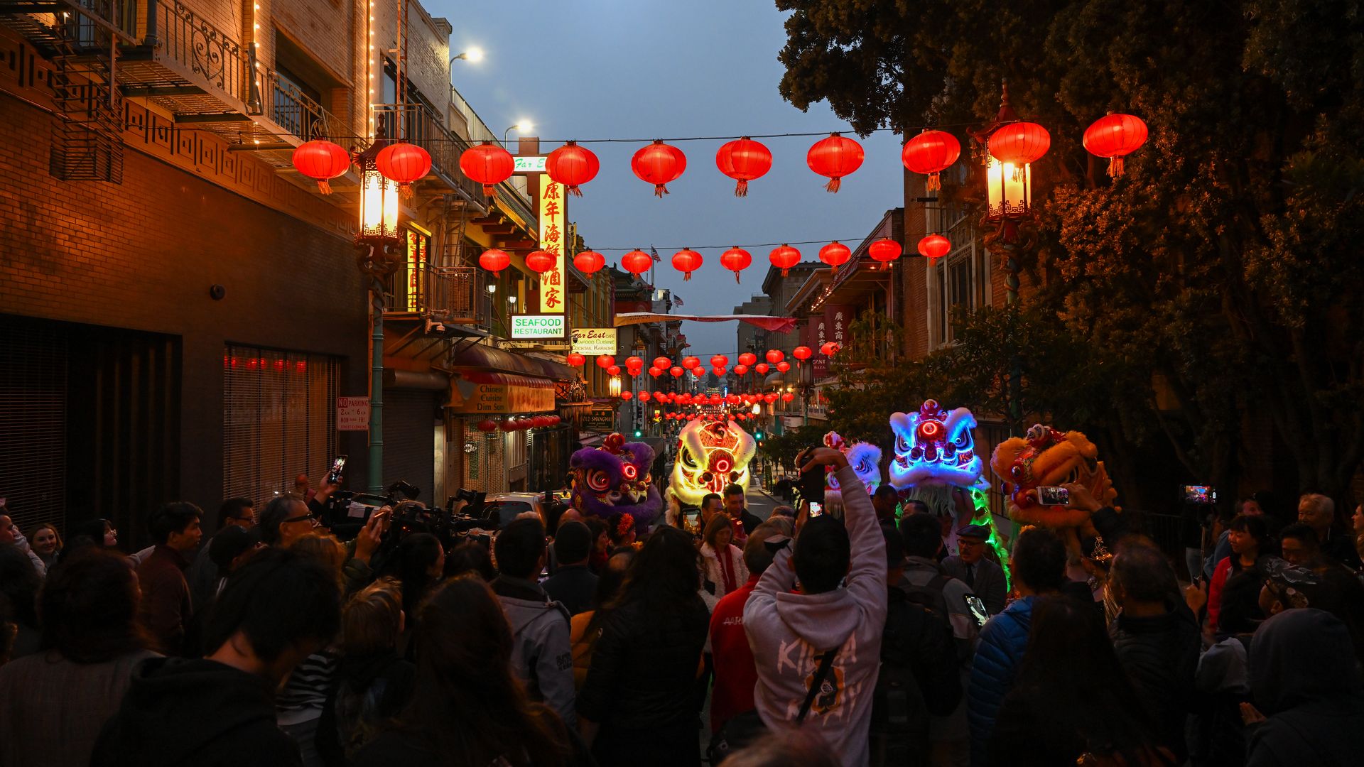 Photo of people standing in a Chinatown street lit up with red lanterns and traditional lion costumes