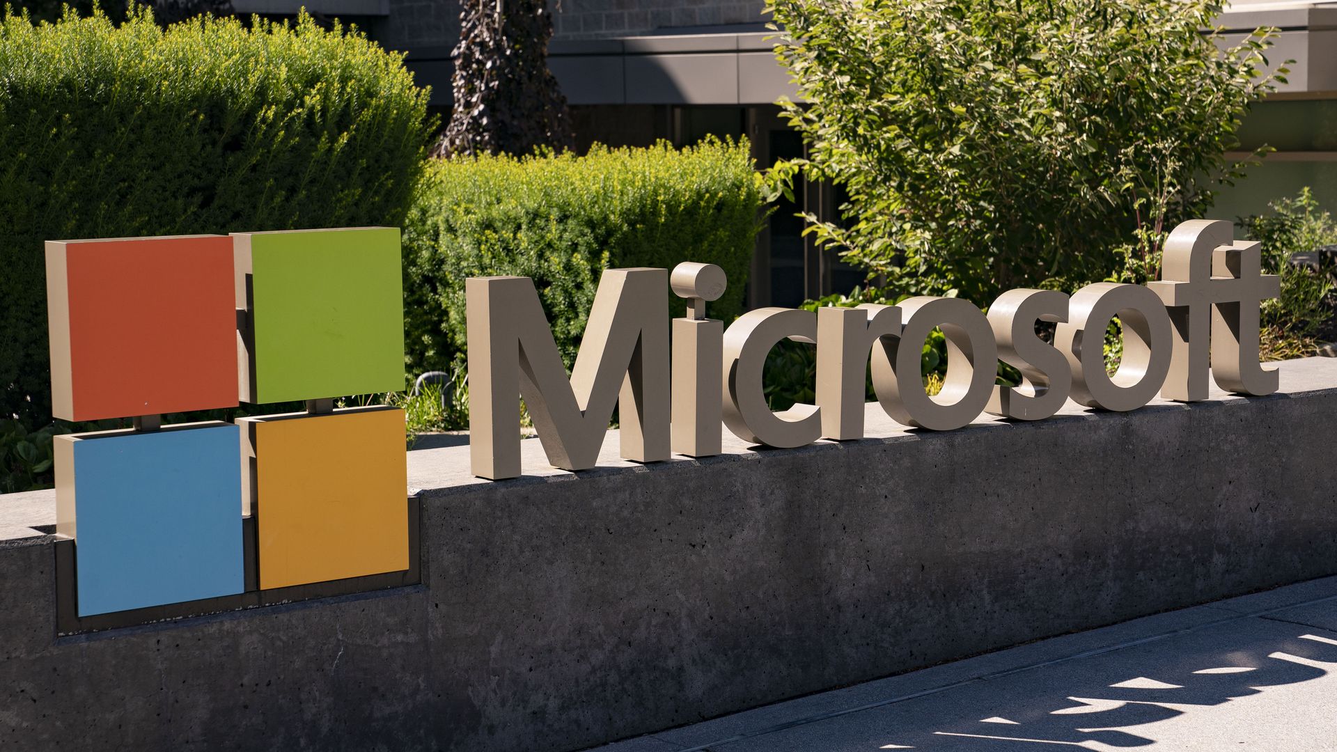 Microsoft's logo and name is shown on a sign outside a building, with green hedges behind the sign.