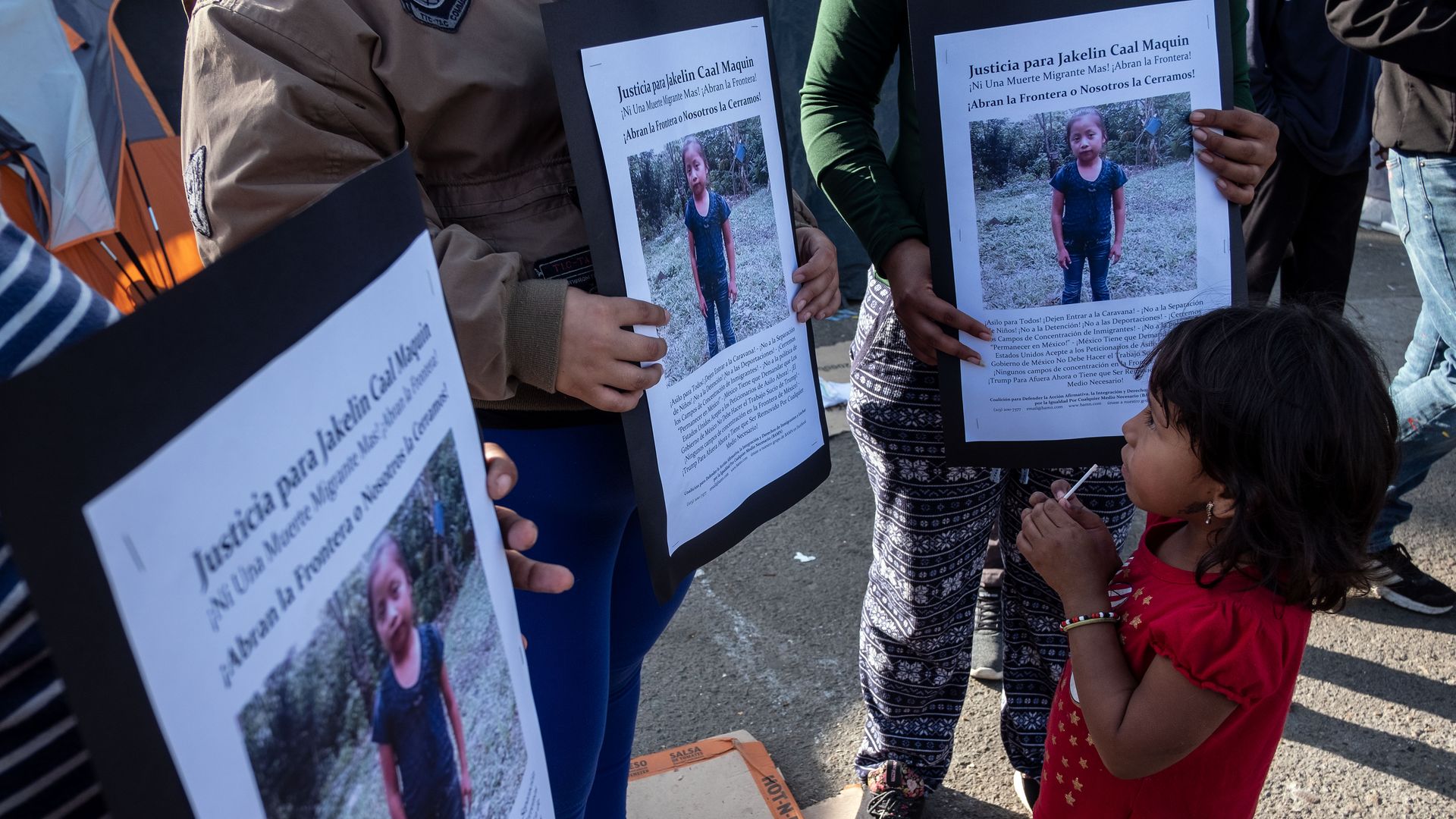 In this image, a child stands in front of demonstrators who hold white text descriptions of missing persons.