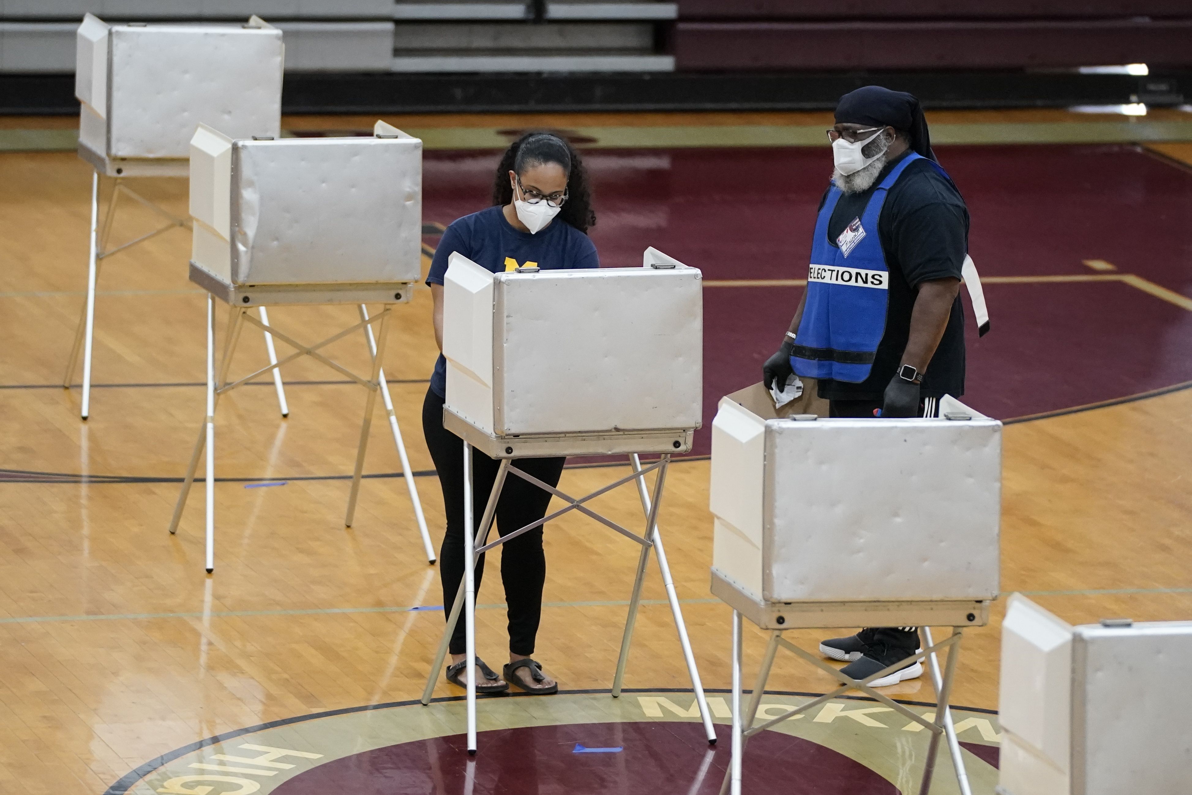 A woman votes in a gym while wearing a face mask
