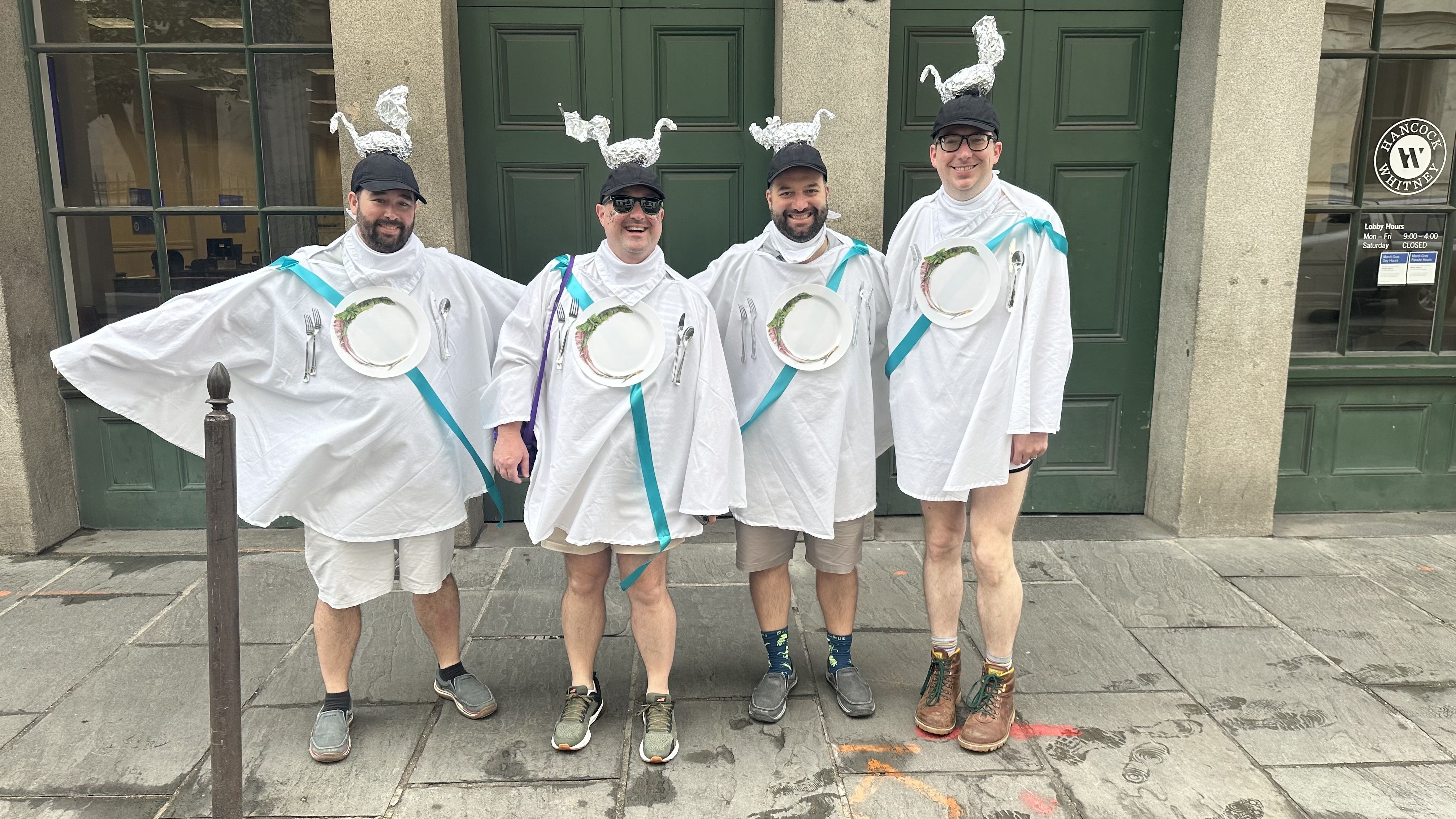 Four people dressed in white capes with aluminum foil swans on their heads.