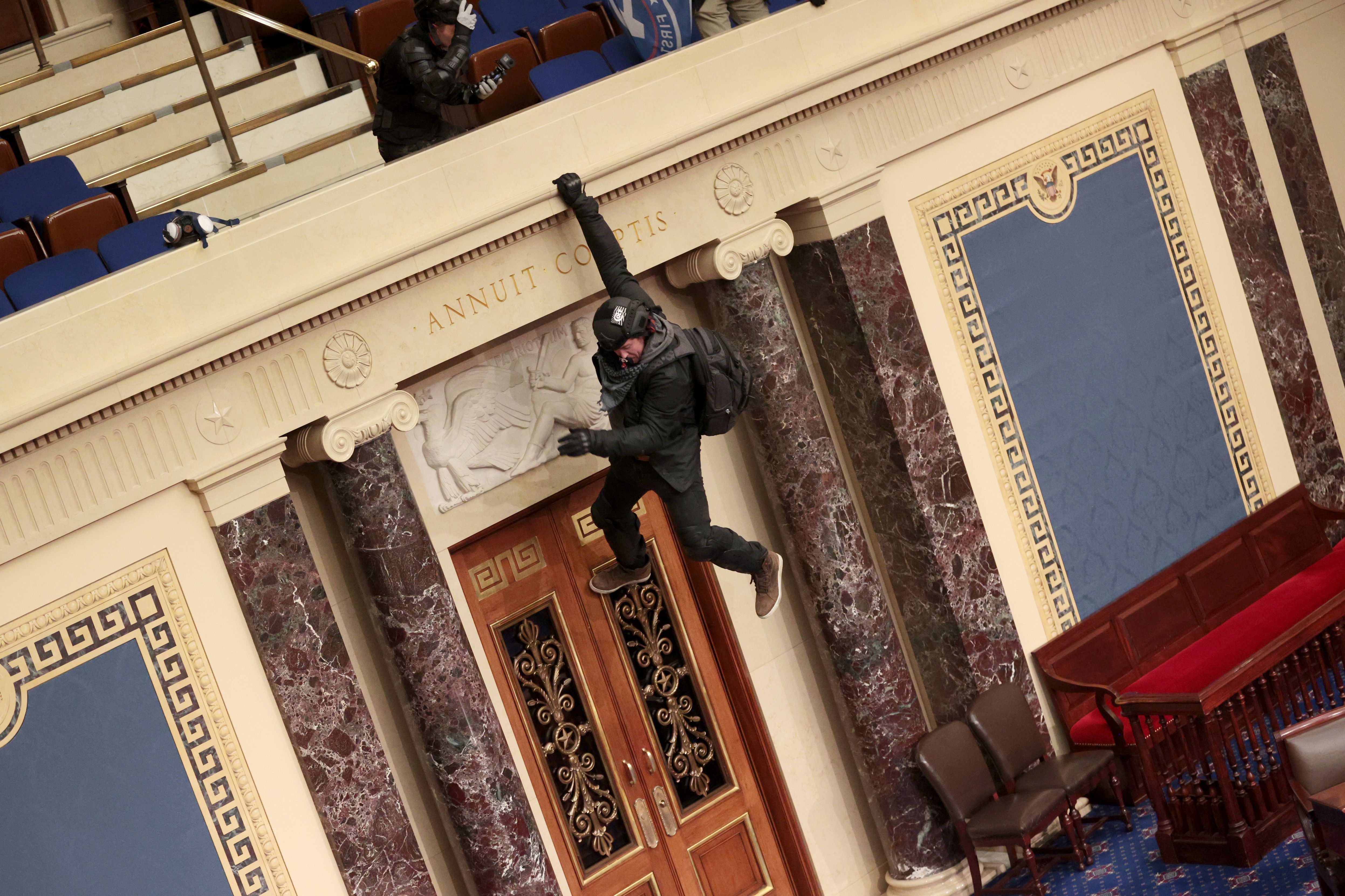 A member of the mob hangs from the balcony in the Senate Chamber.