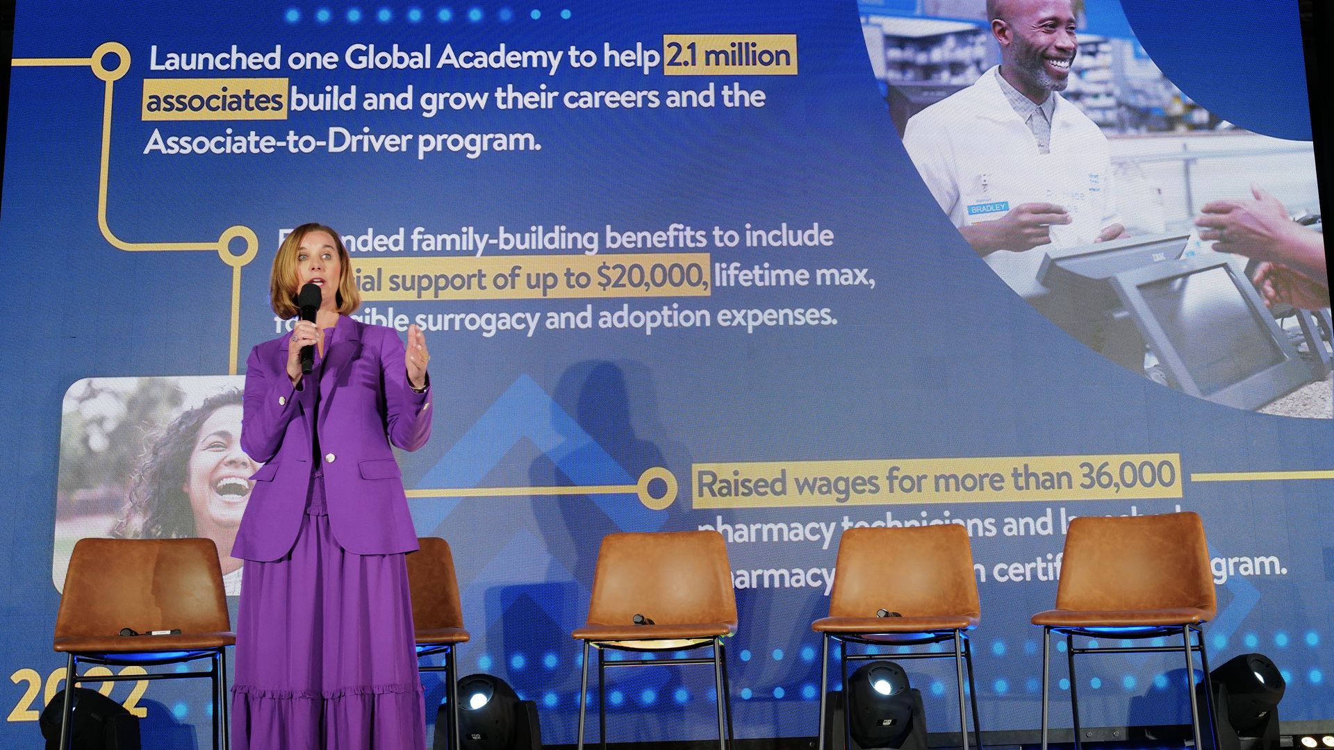 A woman in a purple dress stands on stage and addresses a crowd.