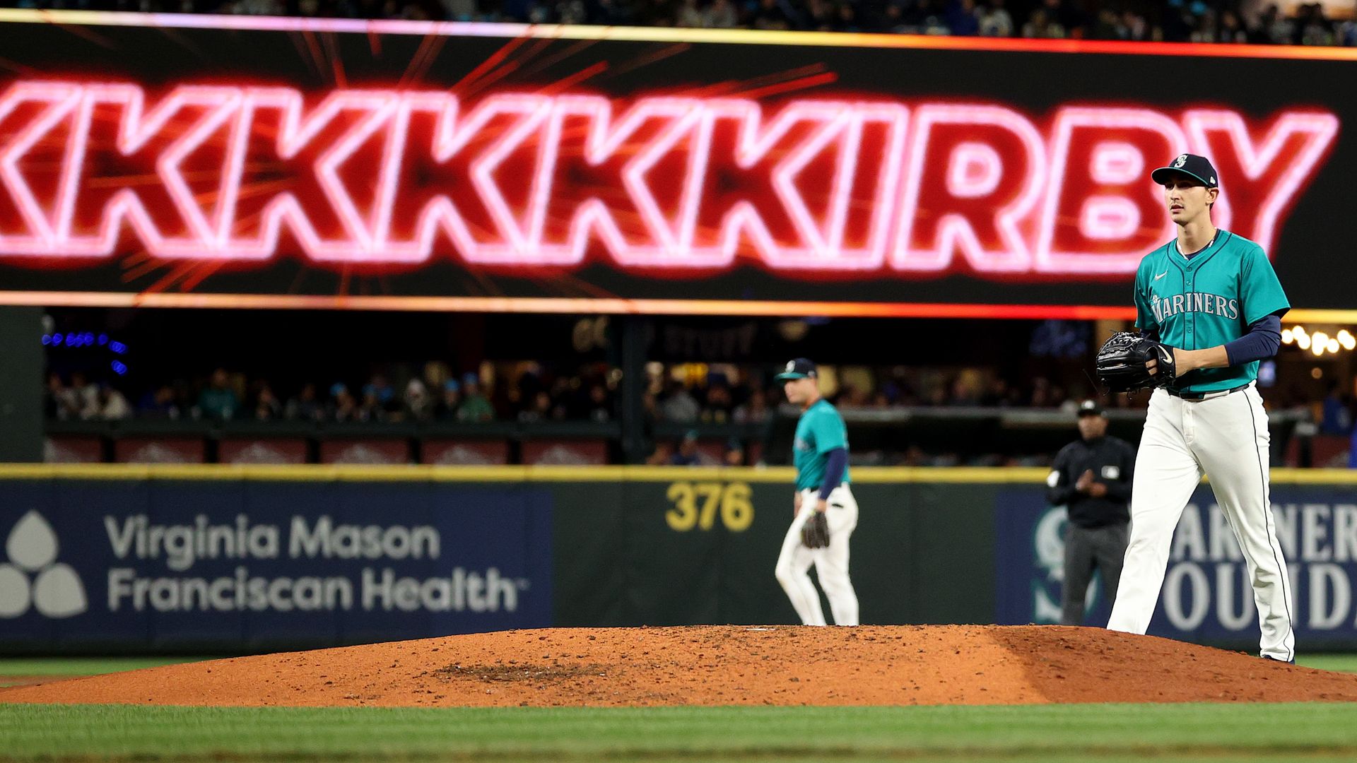 A pitcher walks onto a baseball with his name on a neon sign in the background. 