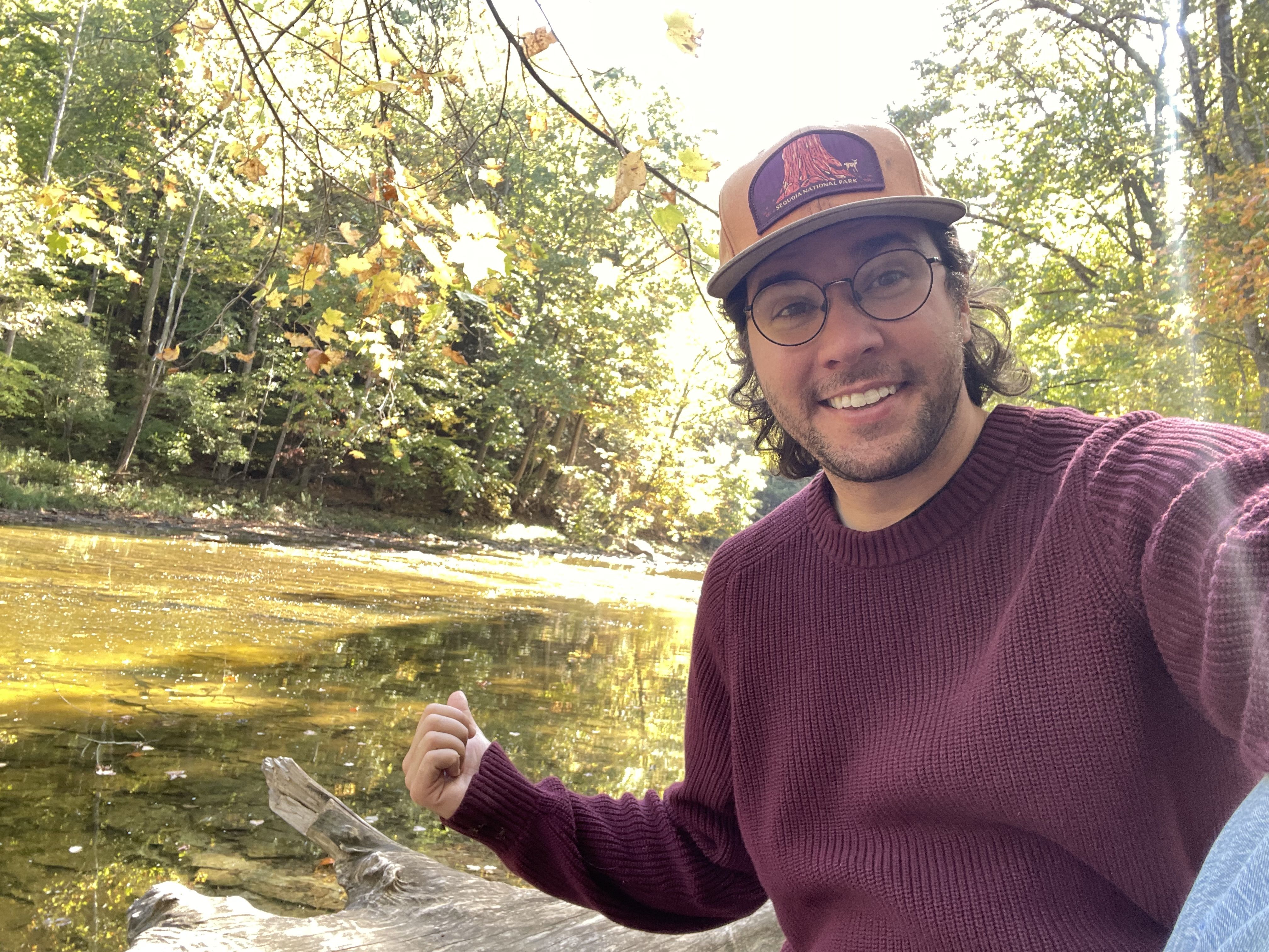 A man in red sweater and orange hat sitting in front of a river.