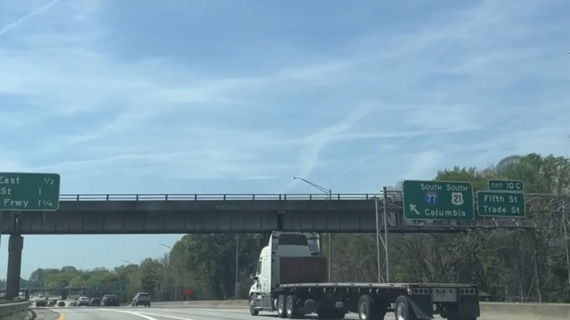 Sunny day on a multi-lane highway; a white semi-trailer sits in the right lane beneath an overpass. Green road signs point to Columbia and list Fifth St and Trade St.
