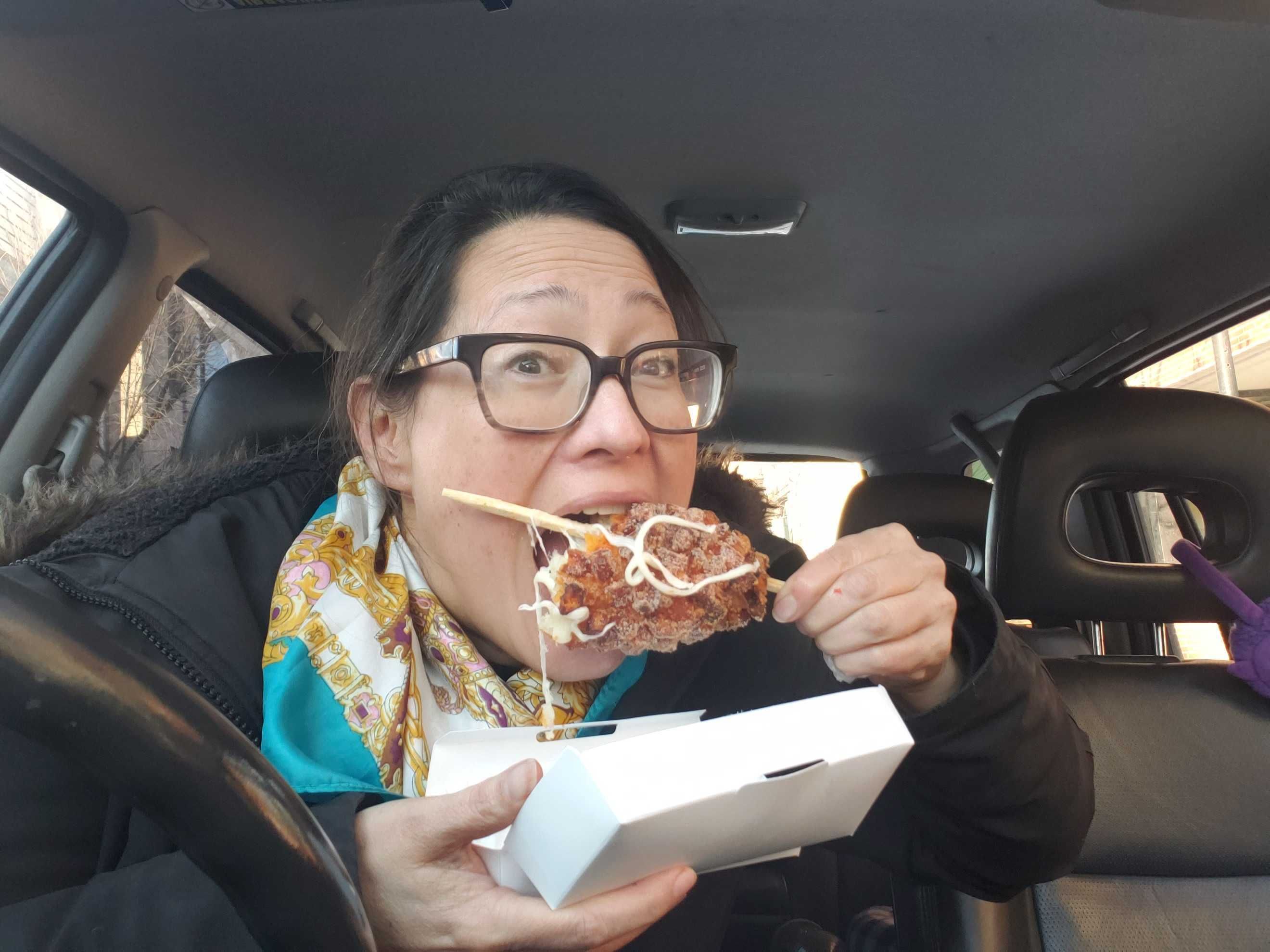Photo of a woman eating a hot dog on a stick. 