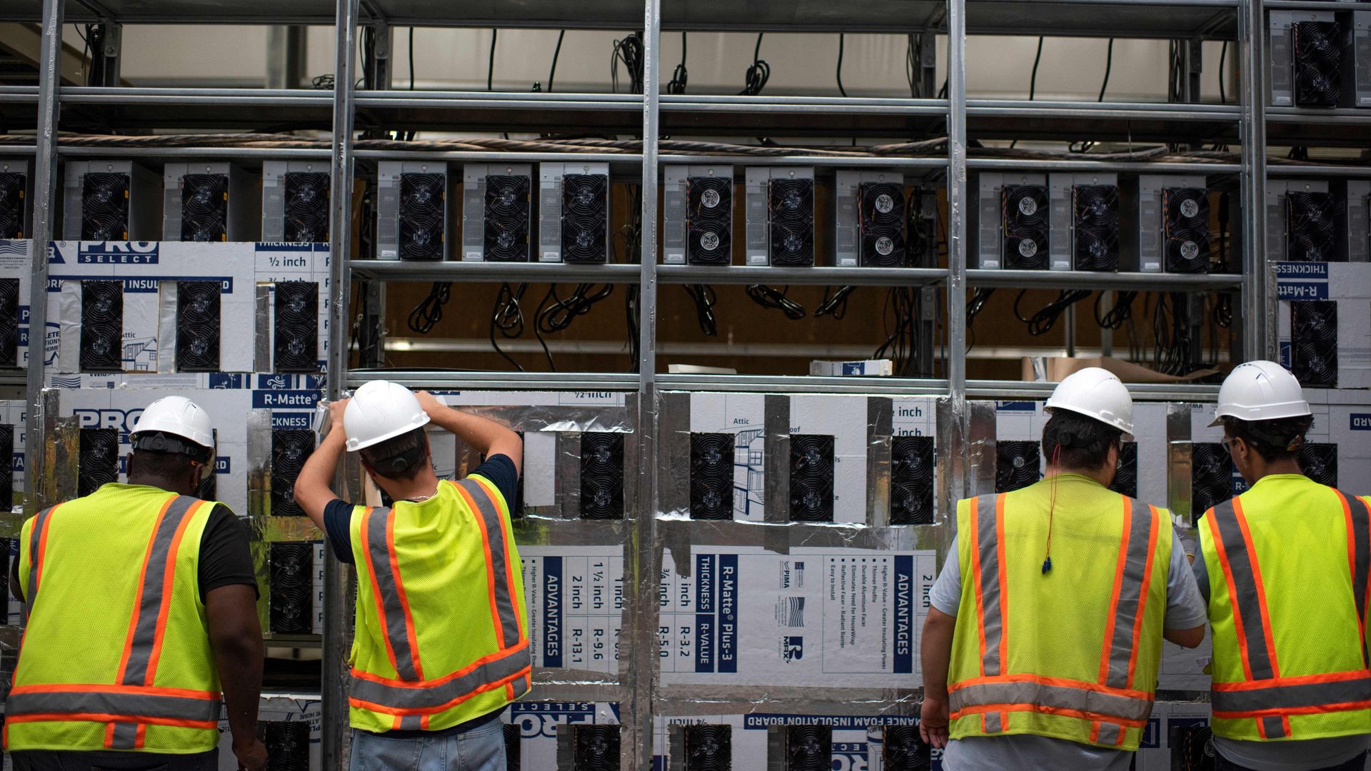 Workers in an data center installing machines, wearing yellow vests and hard hats. 