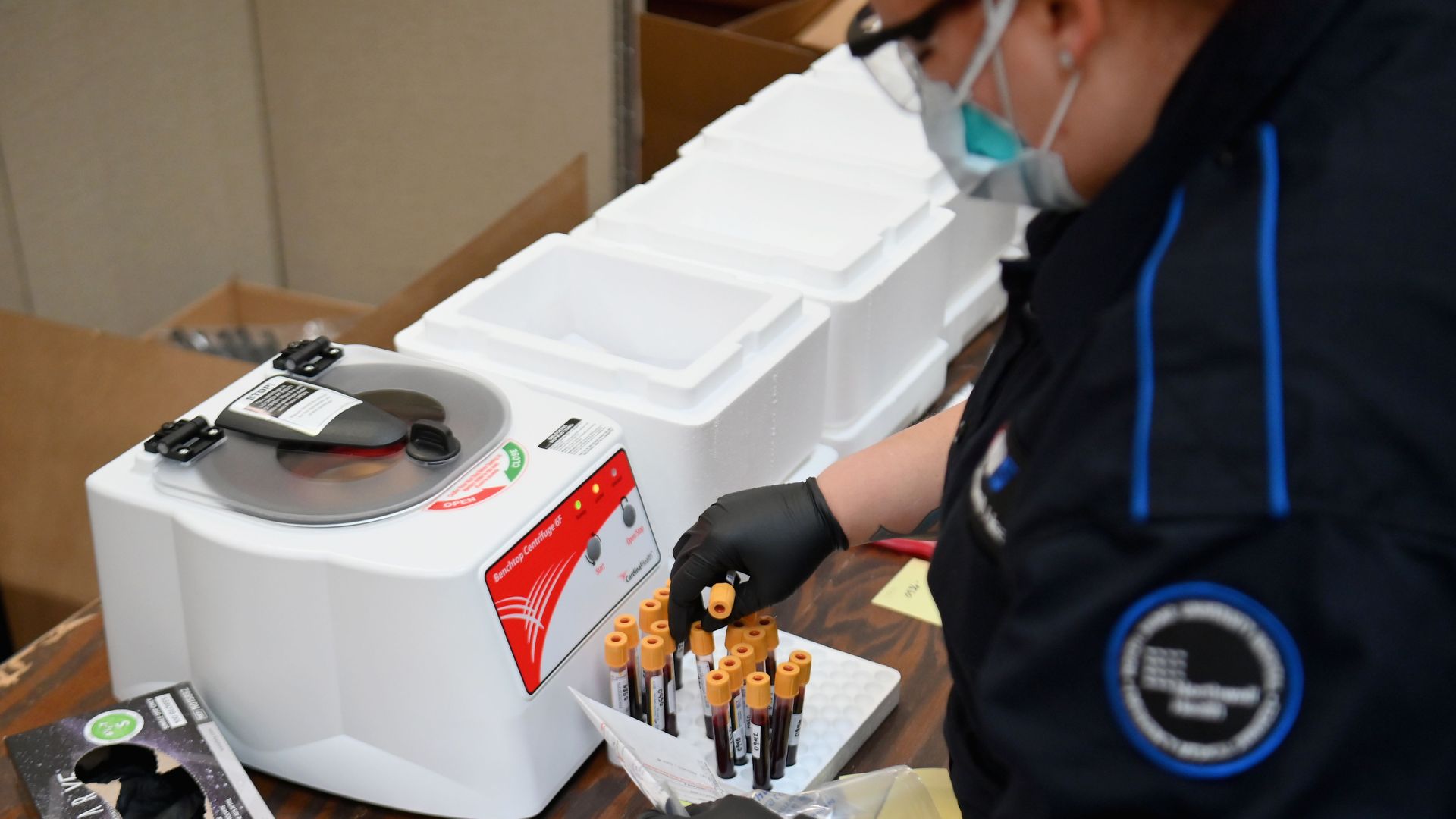 In this image, a woman medical worker handles vials of blood