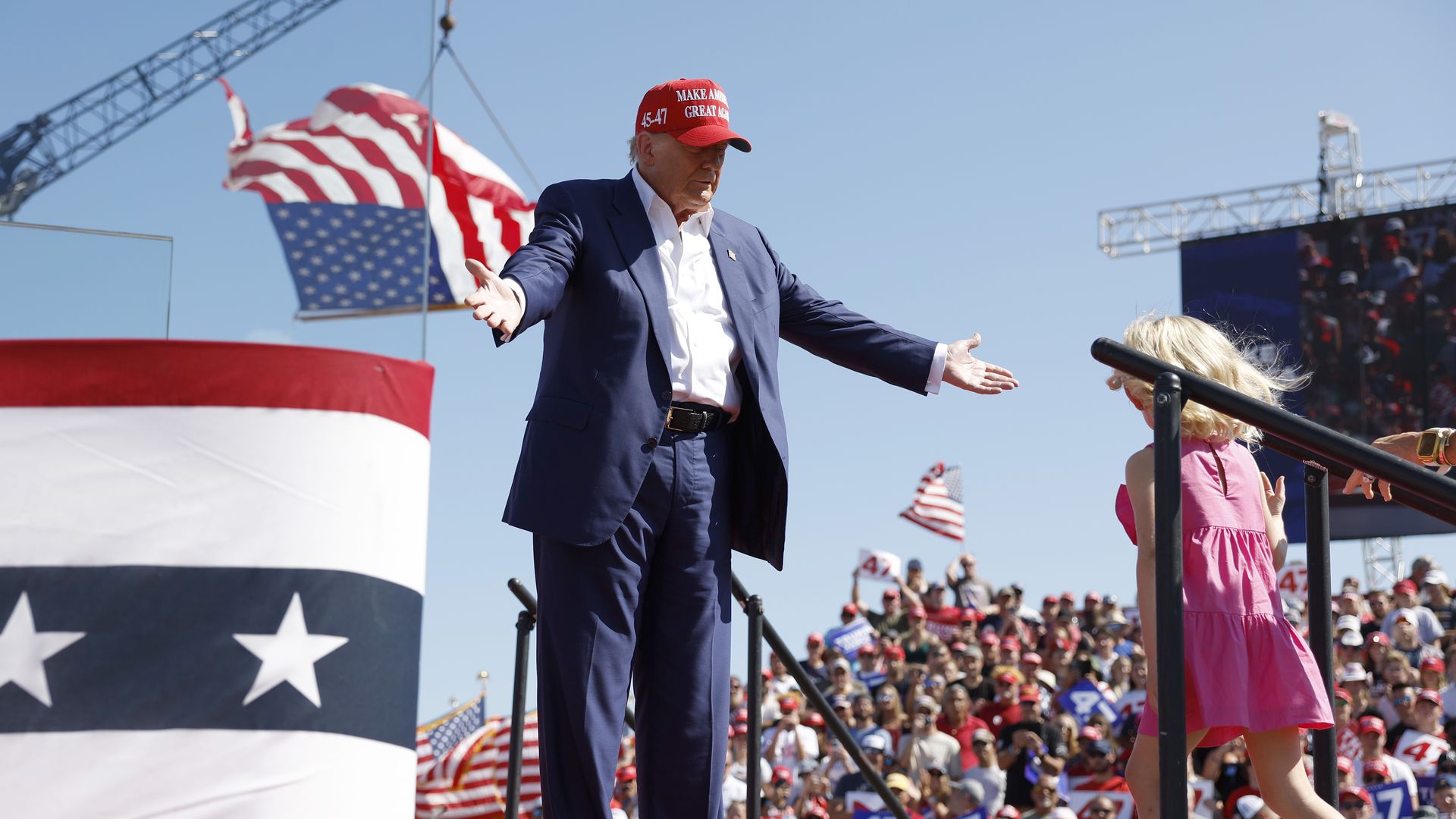 Donald Trump, wearing a blue suit and white shirt, welcomes his granddaughter on stage.