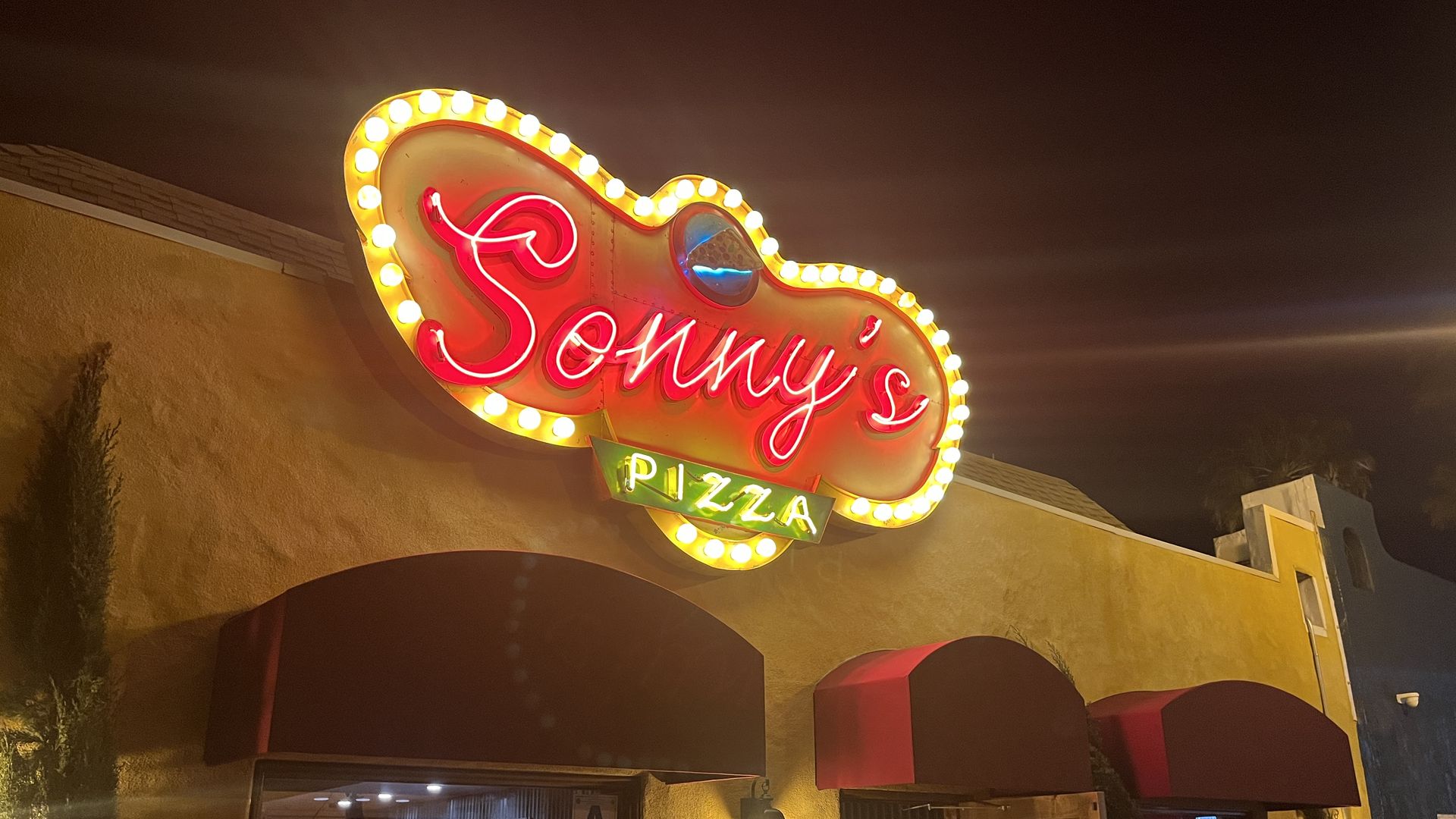 A neon sign that says Sonny's Pizza lights up at a restaurant at night.