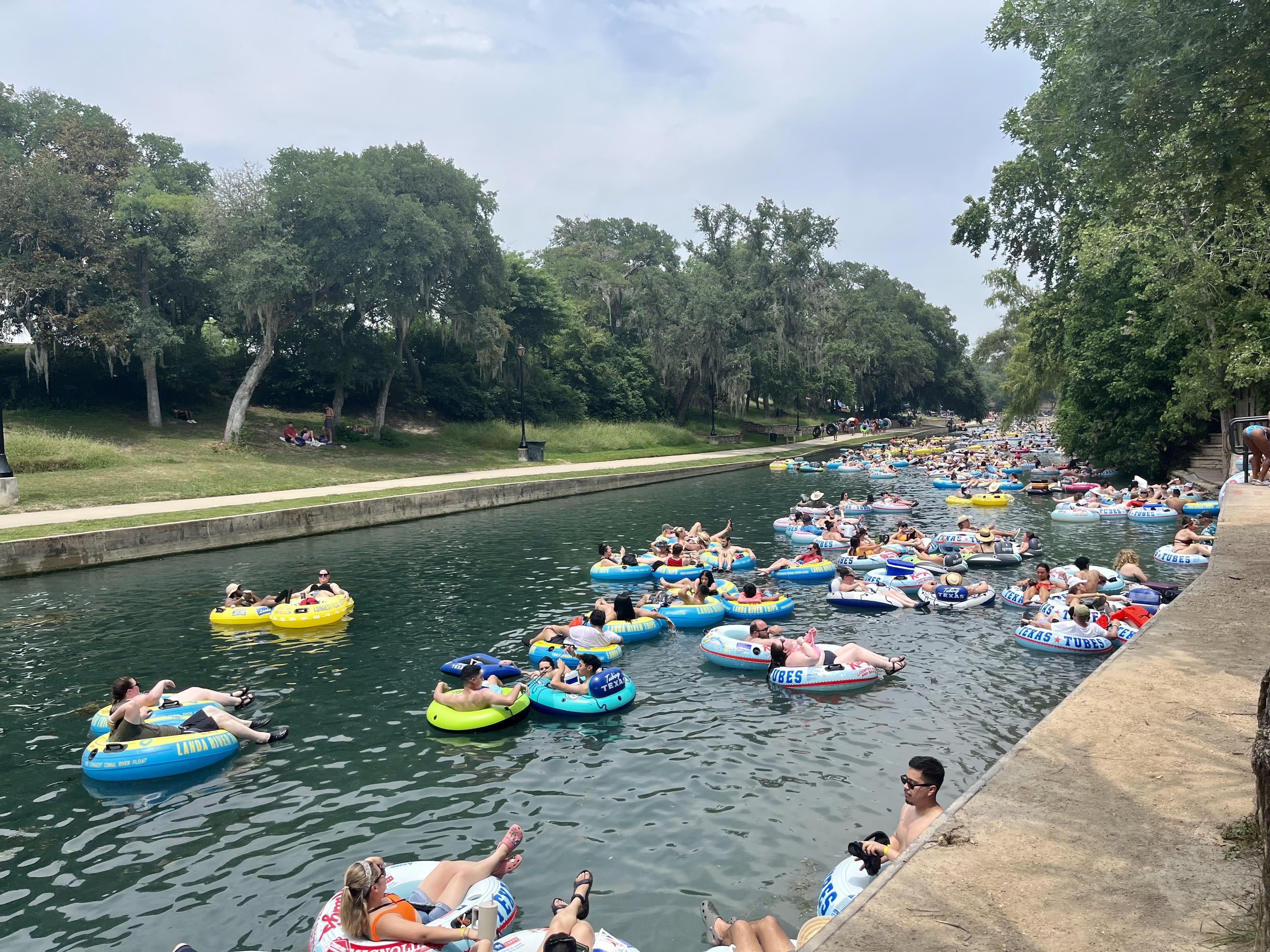 The blue-colored Comal River is filled with people in tubes and framed by trees on both sides.