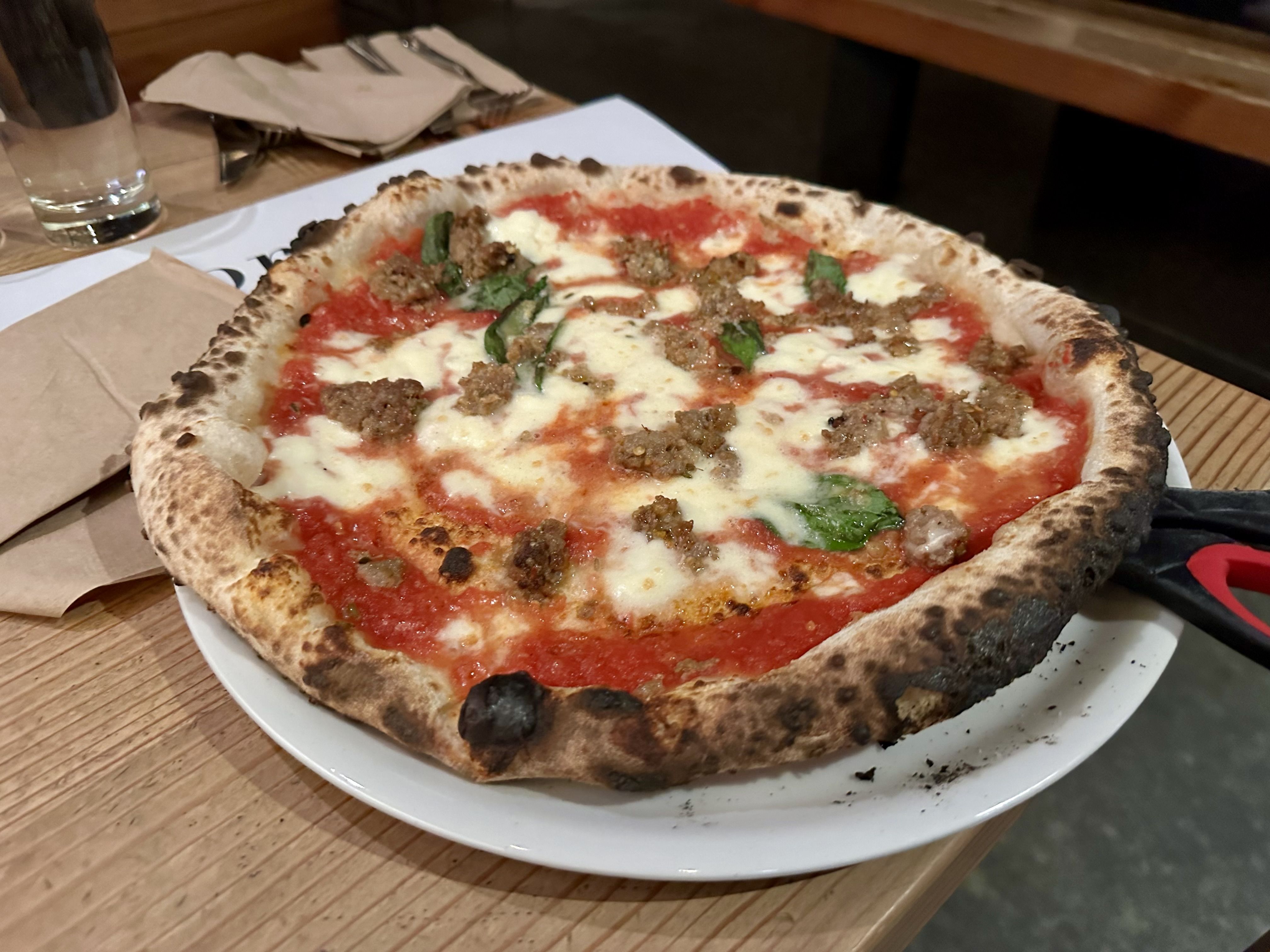 Sausage pizza with basil on it, uncut with scissors provided on a plate. 