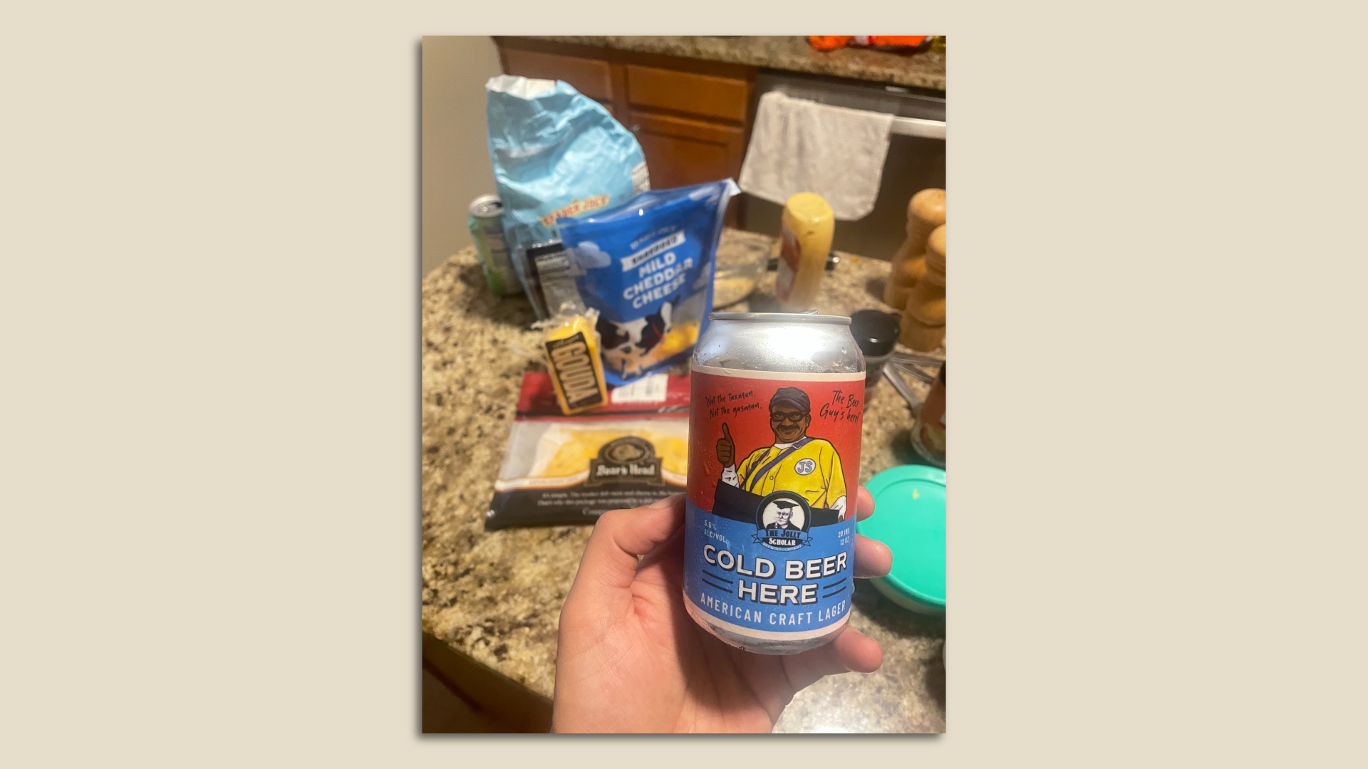 A photo of a can of beer held in front of ingredients for a cheese dip