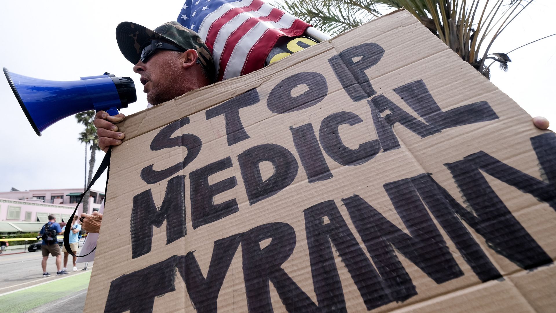 A protester with a bullhorn holds a sign saying "Stop Medical Tyranny."