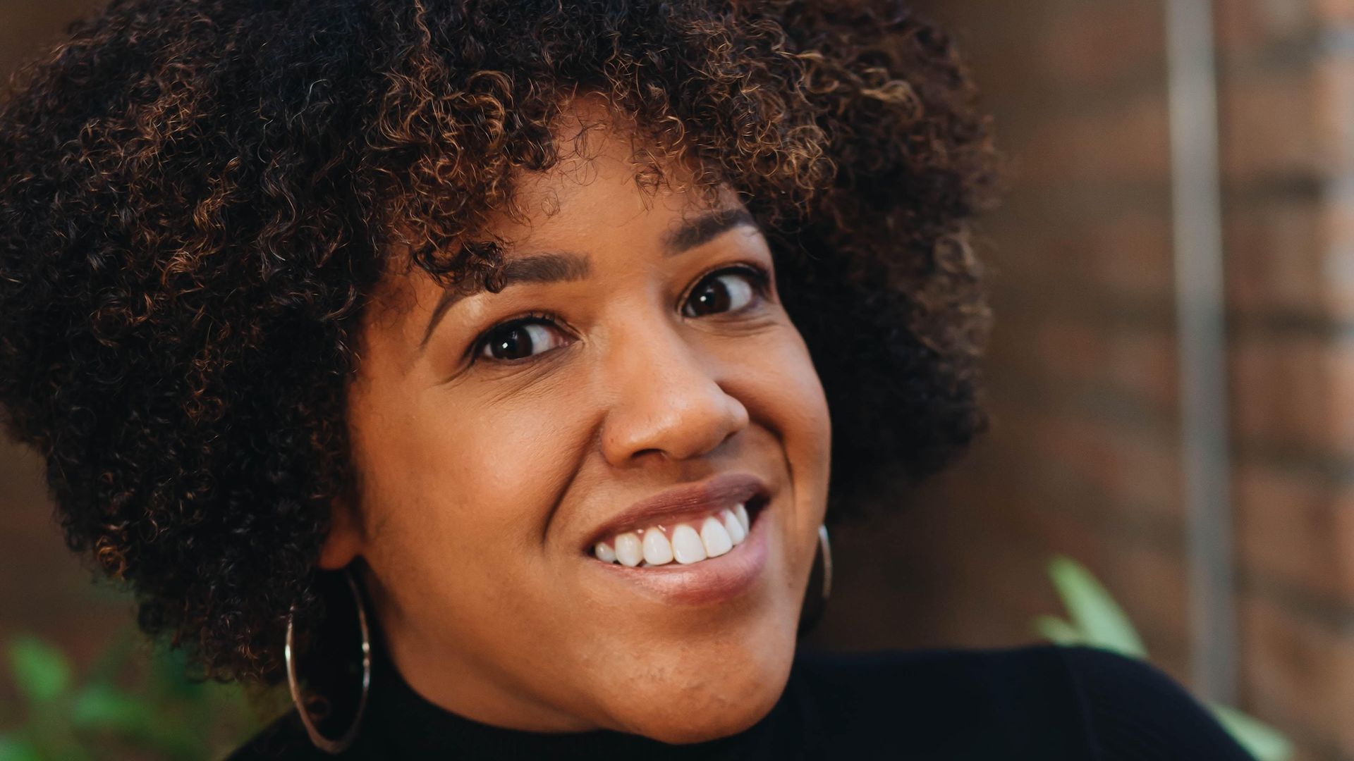 Headshot of woman wearing gold hoop earrings and a black turtleneck.