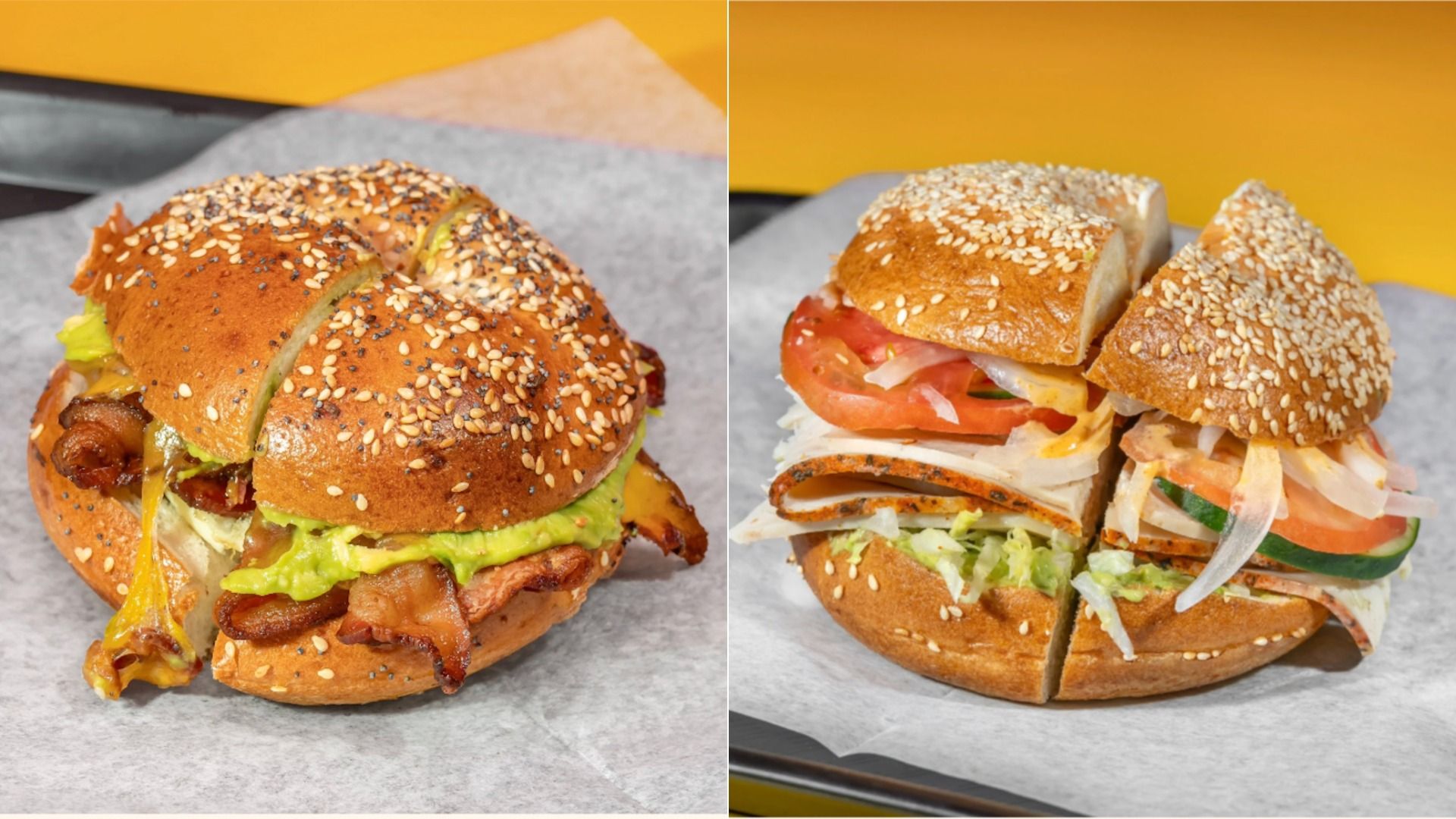 Two sesame seed bagel sandwiches on parchment paper; left has melted cheese, bacon, and guacamole, right has tomato, onion, cucumber, lettuce, and deli meat on sesame bagel.