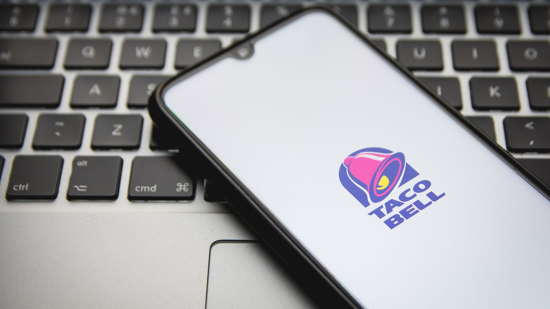 A smartphone displaying the Taco Bell logo sits on a laptop keyboard.