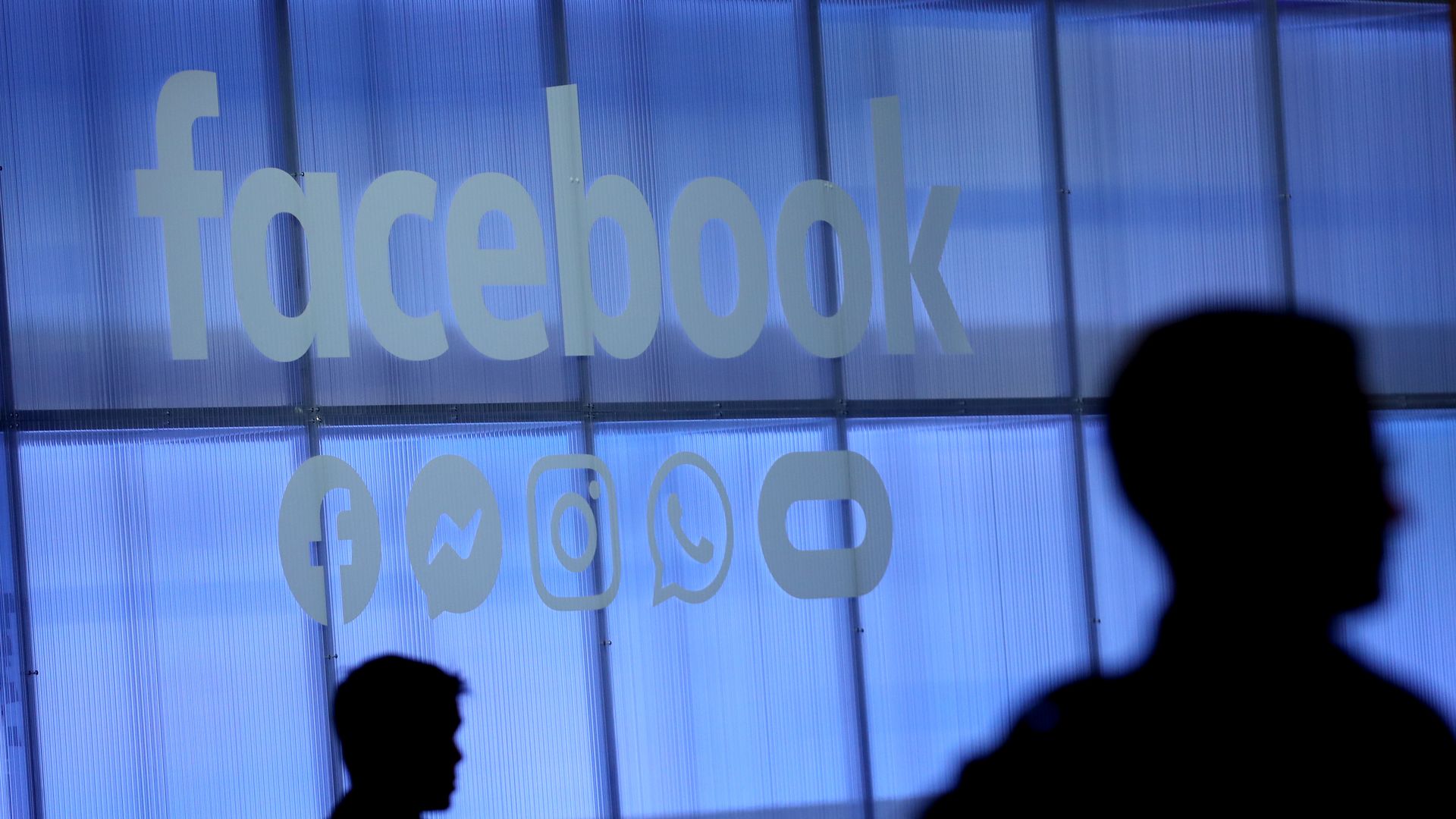 Workers walk past the Facebook logo on an office window