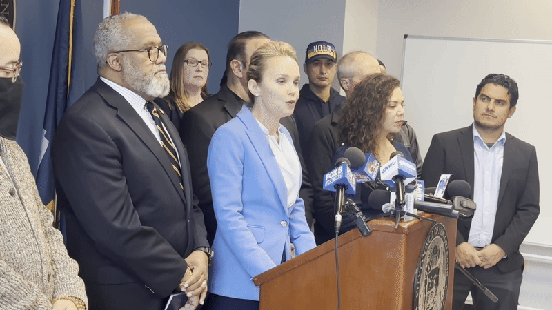 Helena Moreno speaks at a podium in front of a crowd of people including Councilwoman Lesli Harris and Congressman Troy Carter.