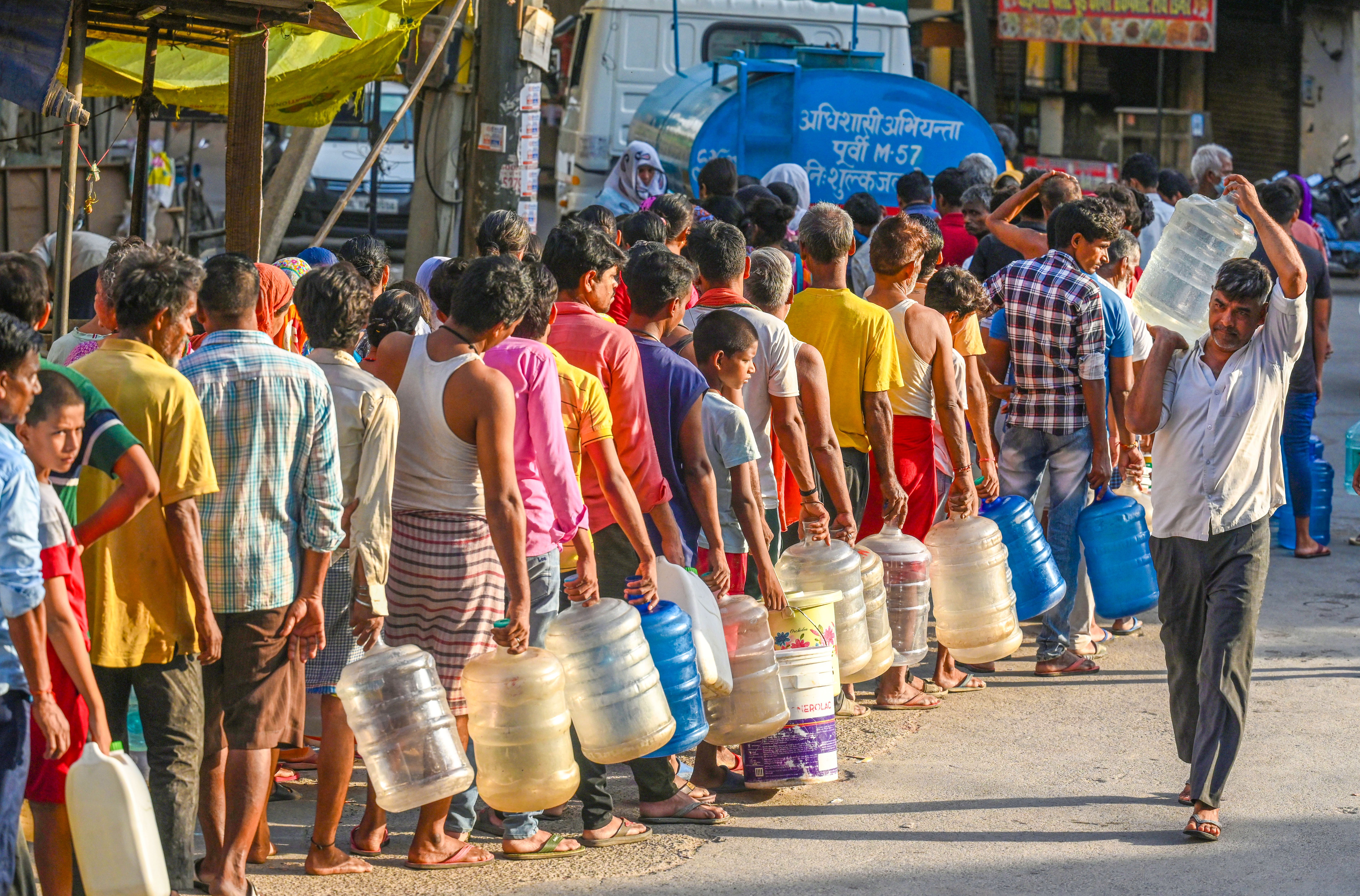 A long line of people waiting for water, everyone is carrying an empty giant jug, sometimes two. 