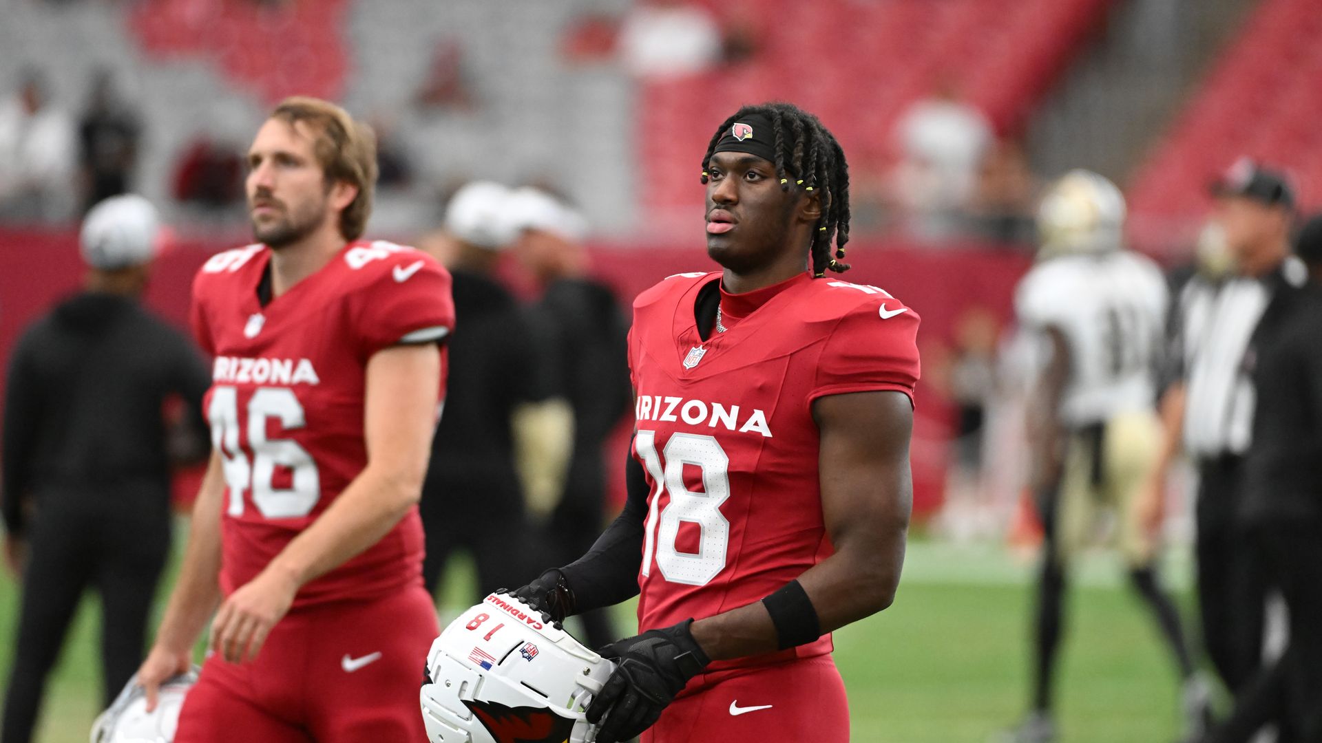 Arizona Cardinals player Marvin Harrison Junior stands on a football field holding his helmet.