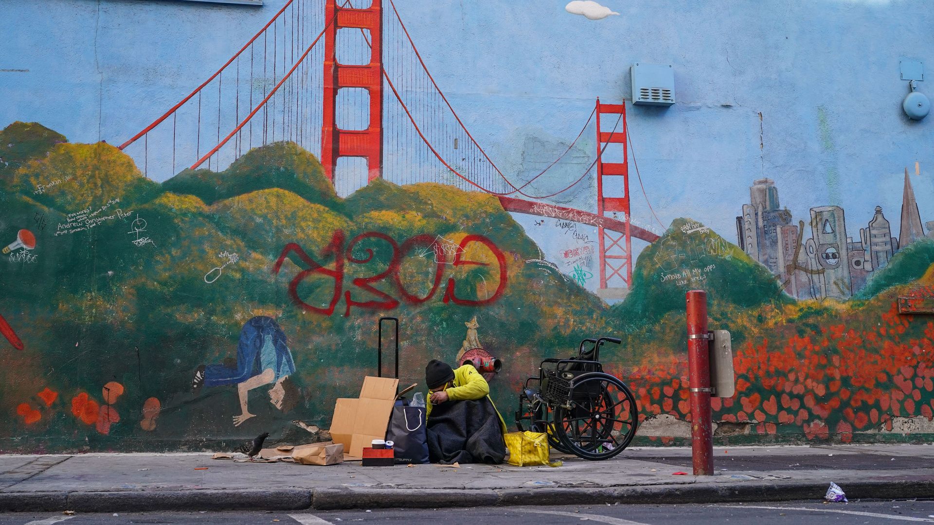 Photo of a homeless person sitting next to a mural of the Golden Gate Bridge