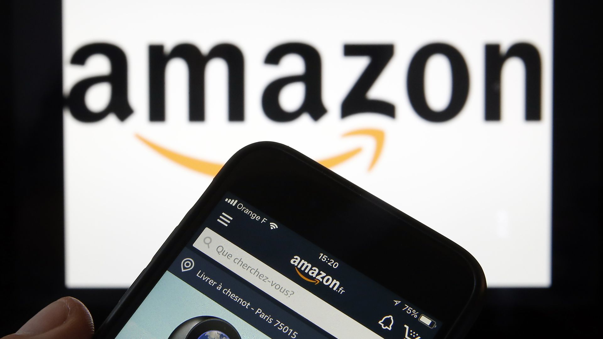 Amazon's logo in the background with the Amazon website on a phone in the foreground.