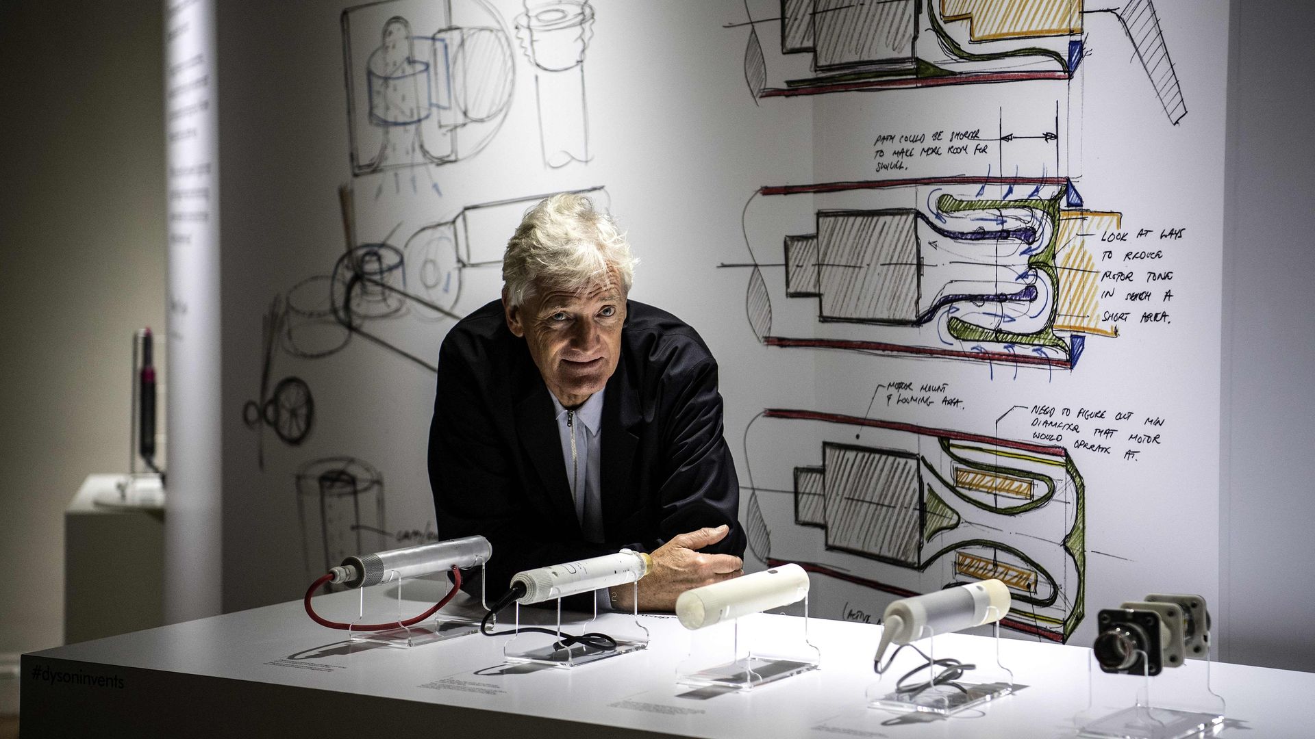 Dyson ceo leaning on a table with blueprints of vacuums. 