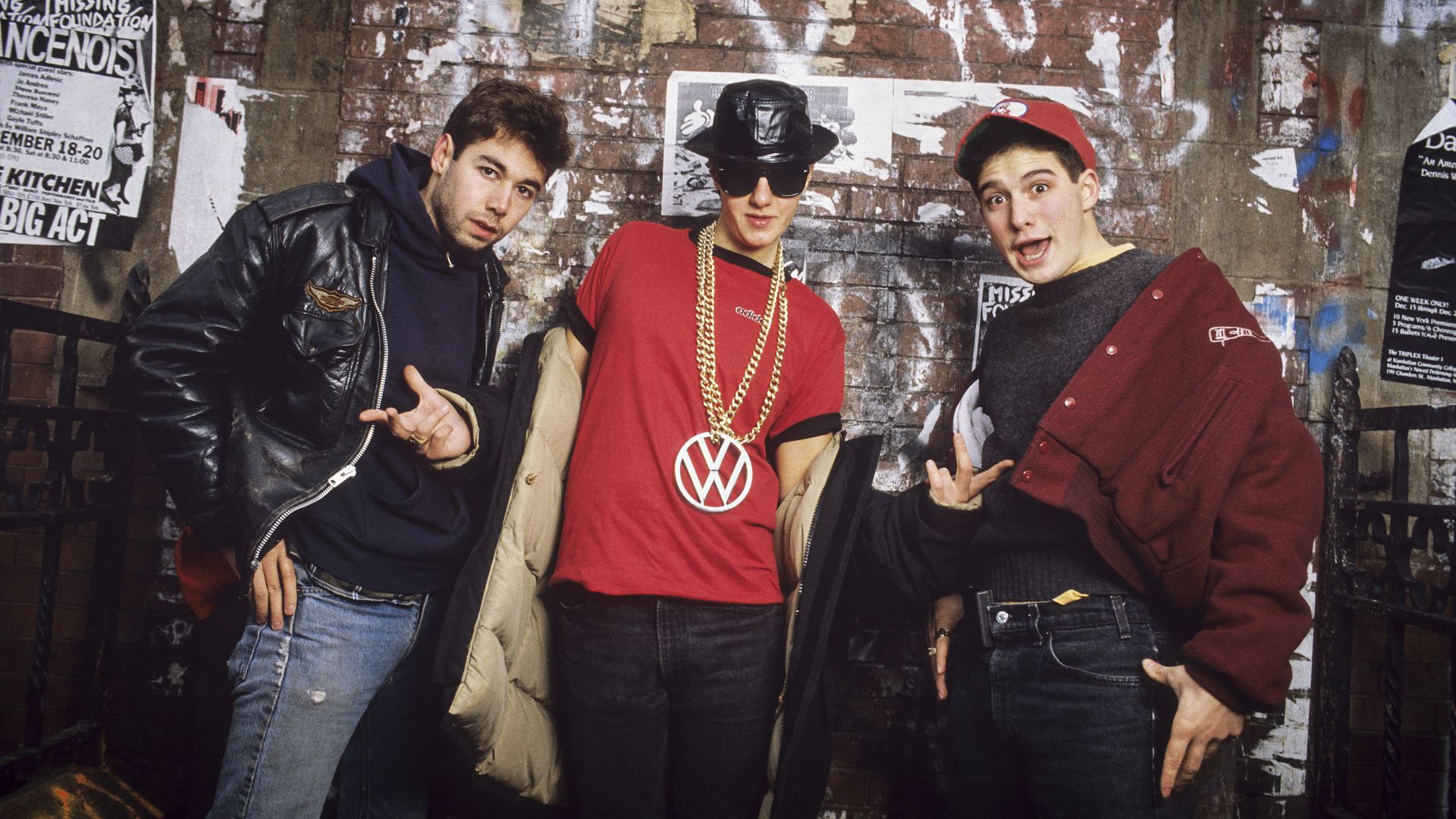 Three men face the camera wearing jackets and jeans