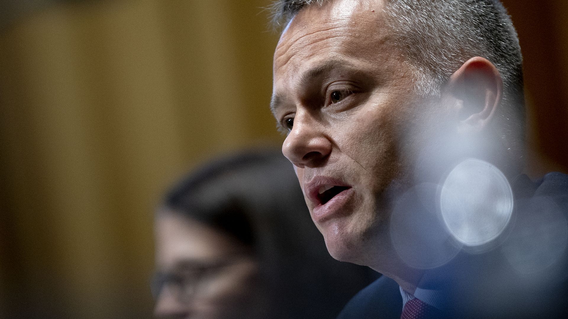 A man, not quite in full profile, appears to either breathe or speak in congressional testimony.