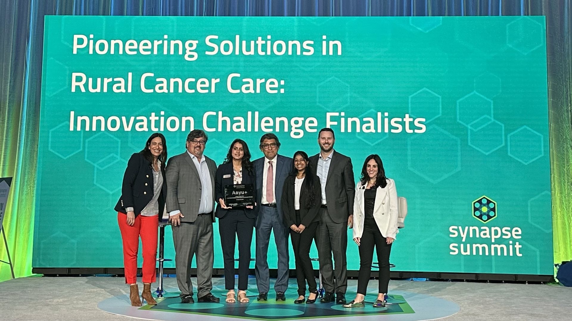 Finalists for the Synapse Summit's Innovation Challenge pose together on stage.