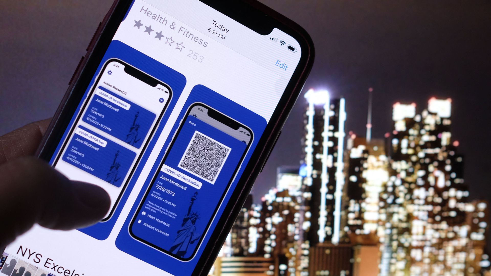 A person looking at the app for the New York State Excelsior Pass, which provides secure, digital proof of a Covid-19 vaccination, in front of a screen showing the New York skyline.