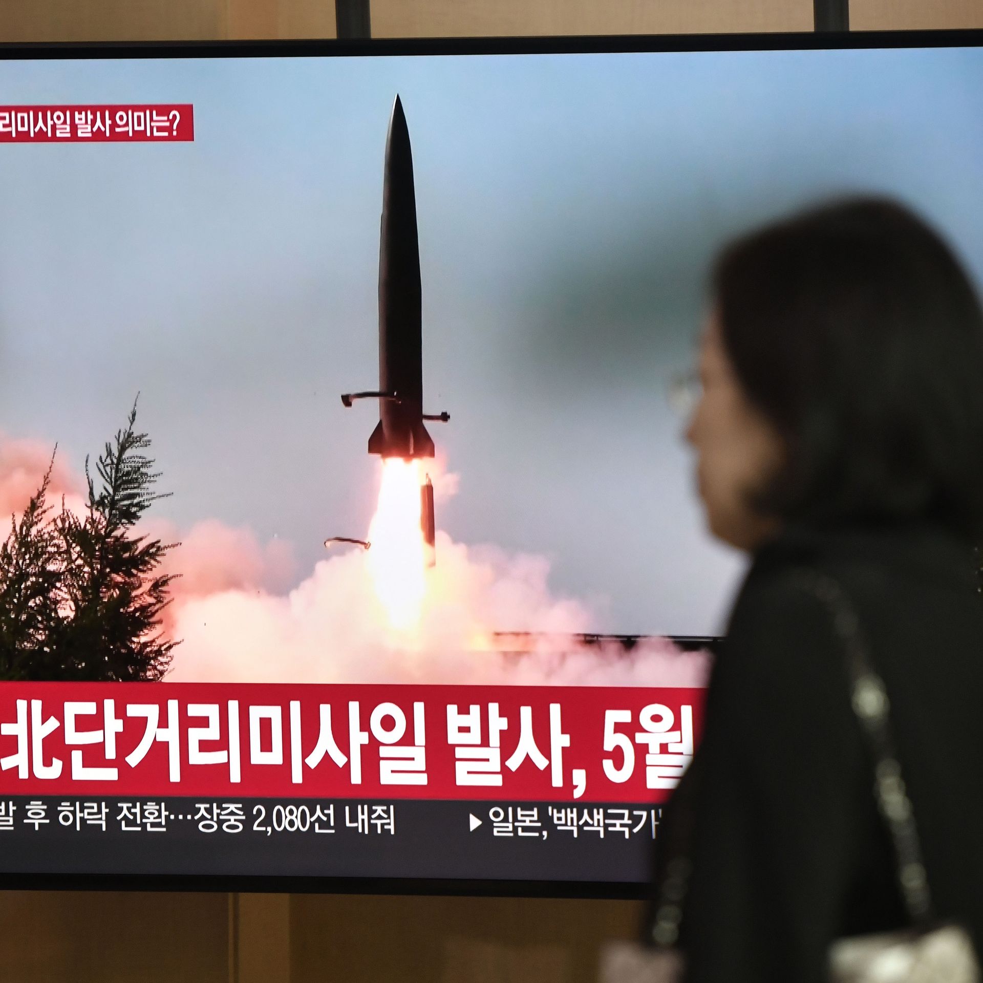 woman standing next to a television showing a missile launch