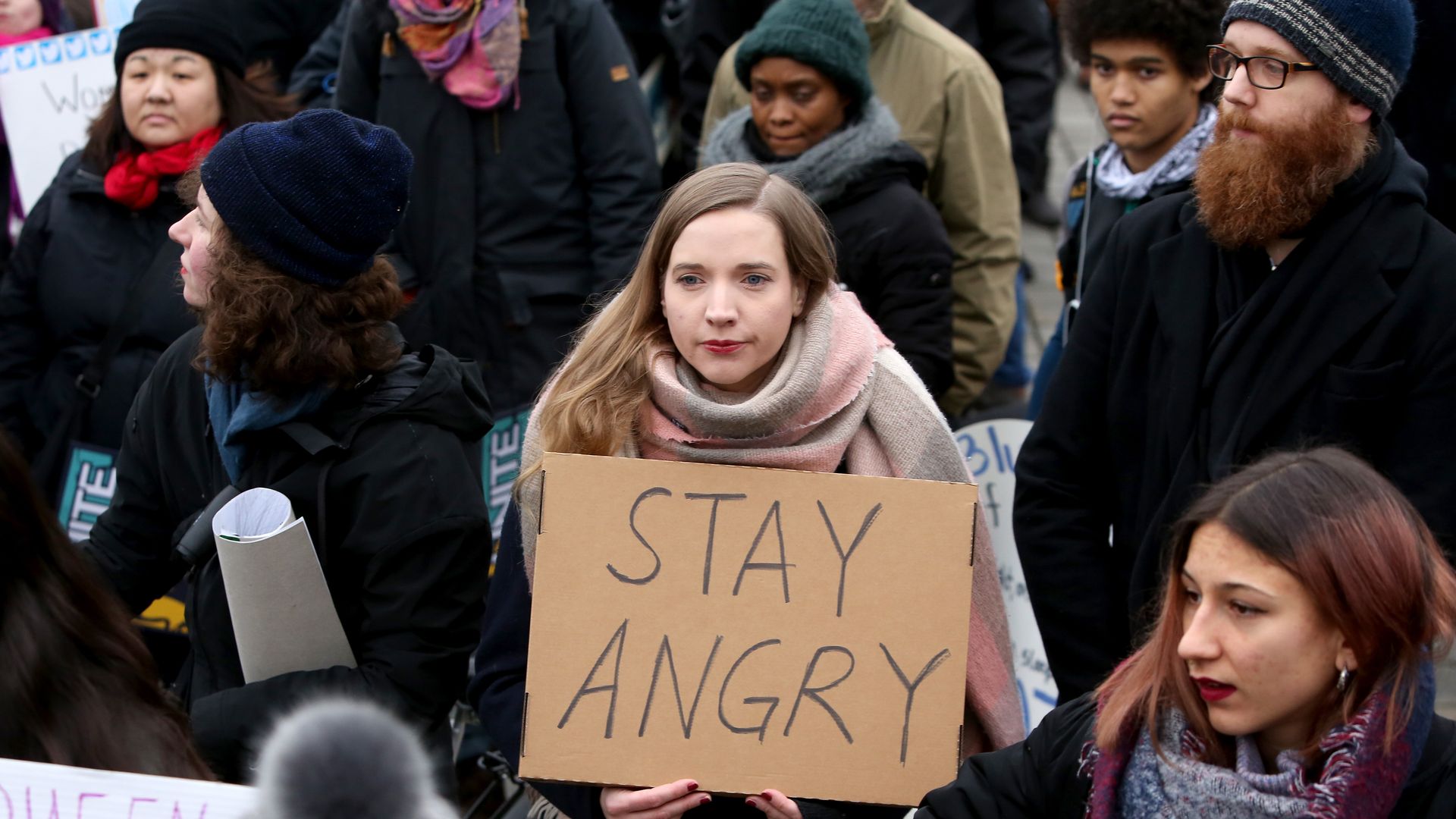 A woman holds a sign that says "Stay angry"
