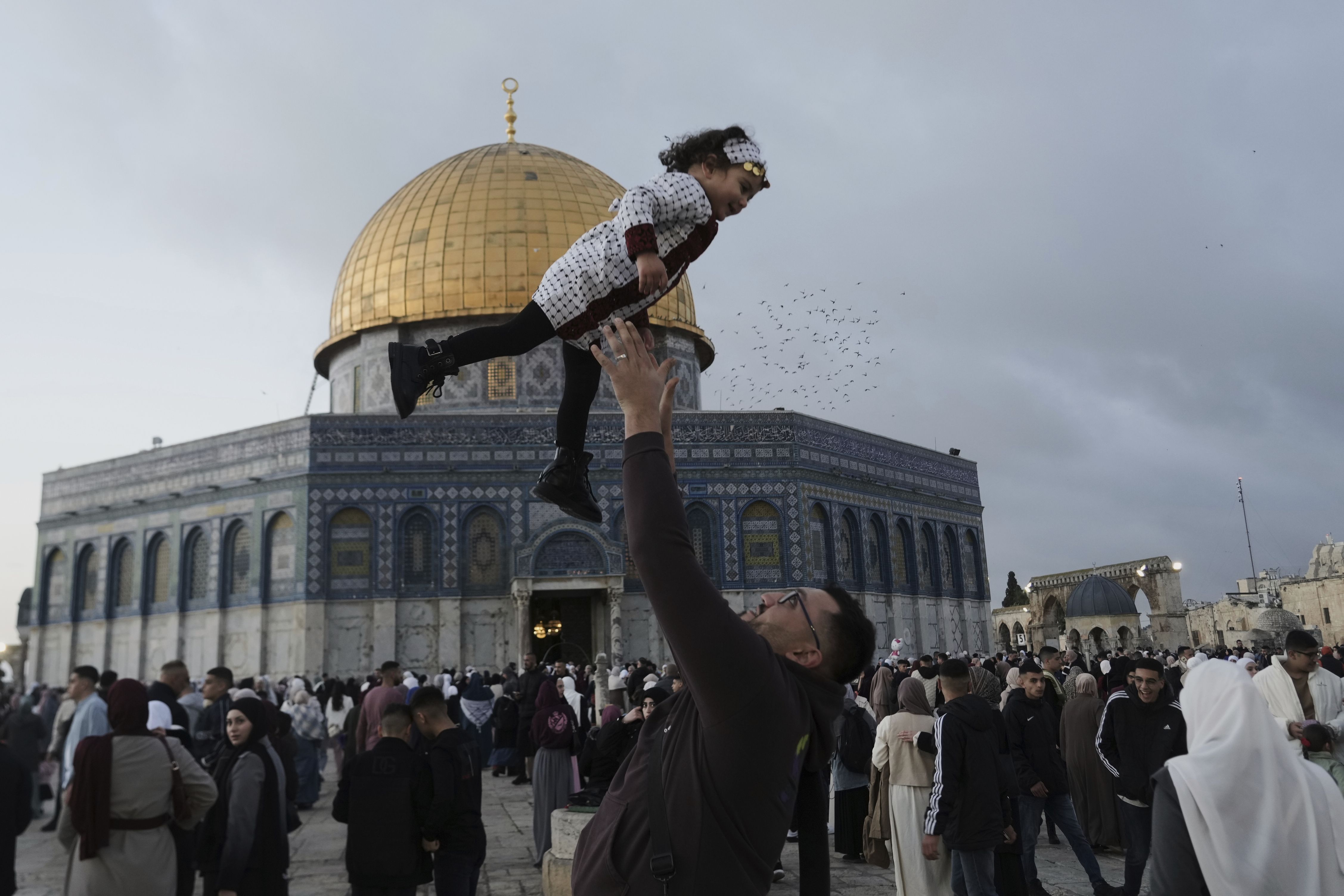 A man throws a smiling girl into the air outside a mosque