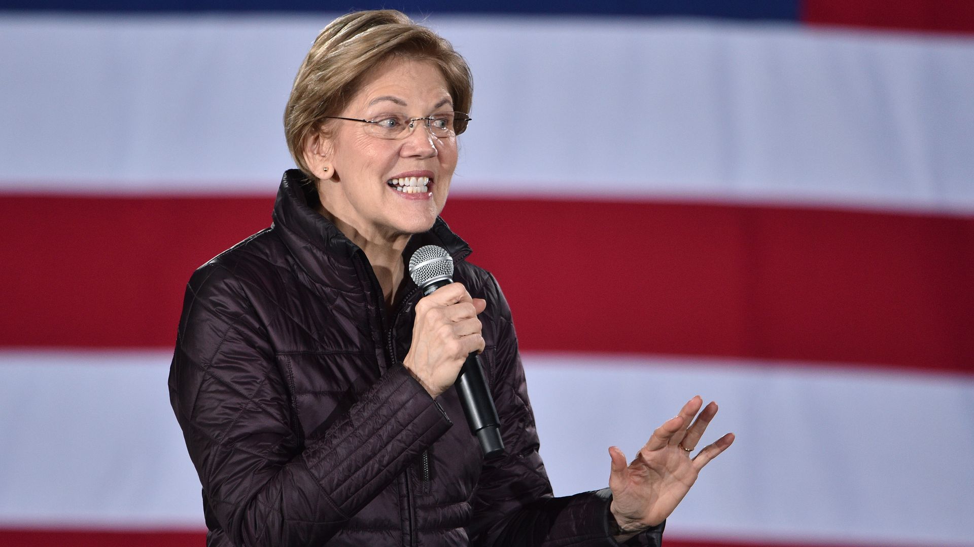 In this image, Elizabeth Warren holds a microphone and speaks
