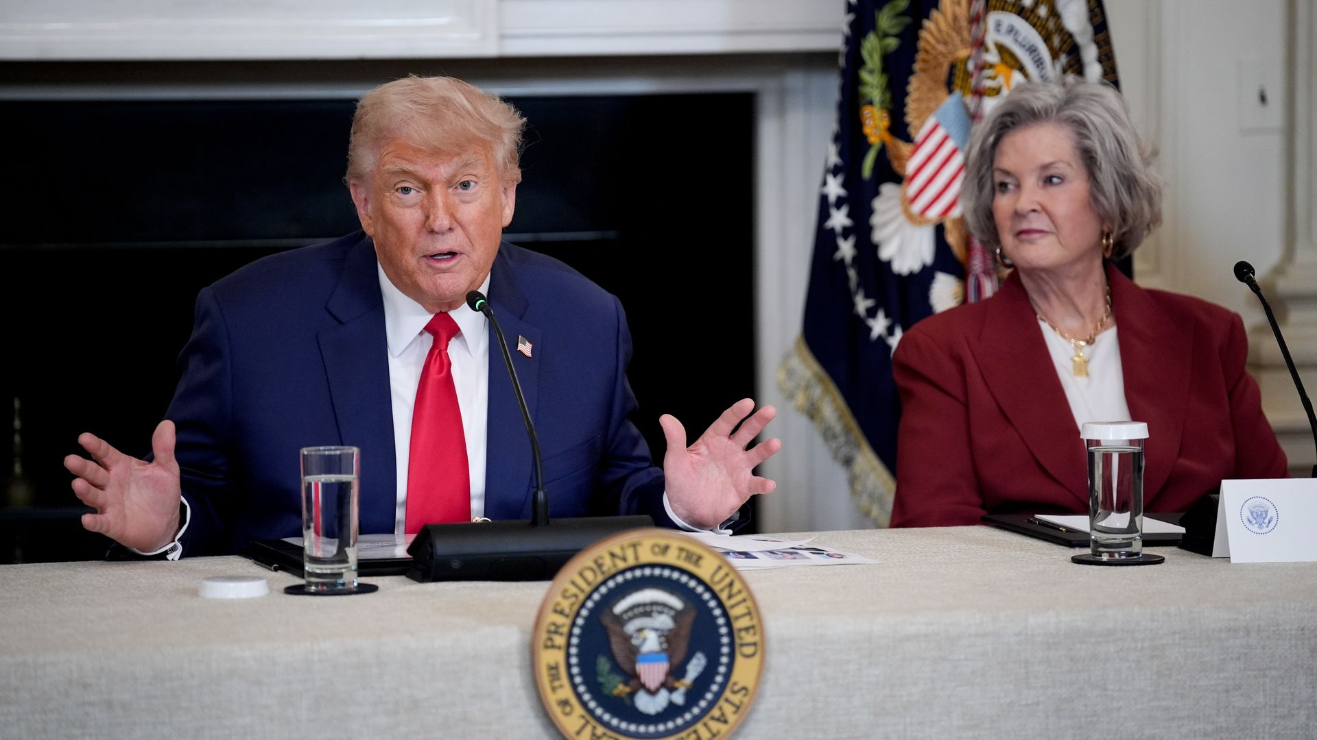 U.S. President Donald Trump gestures while speaking from a table with chief of staff Susie Wiles seated to his left.